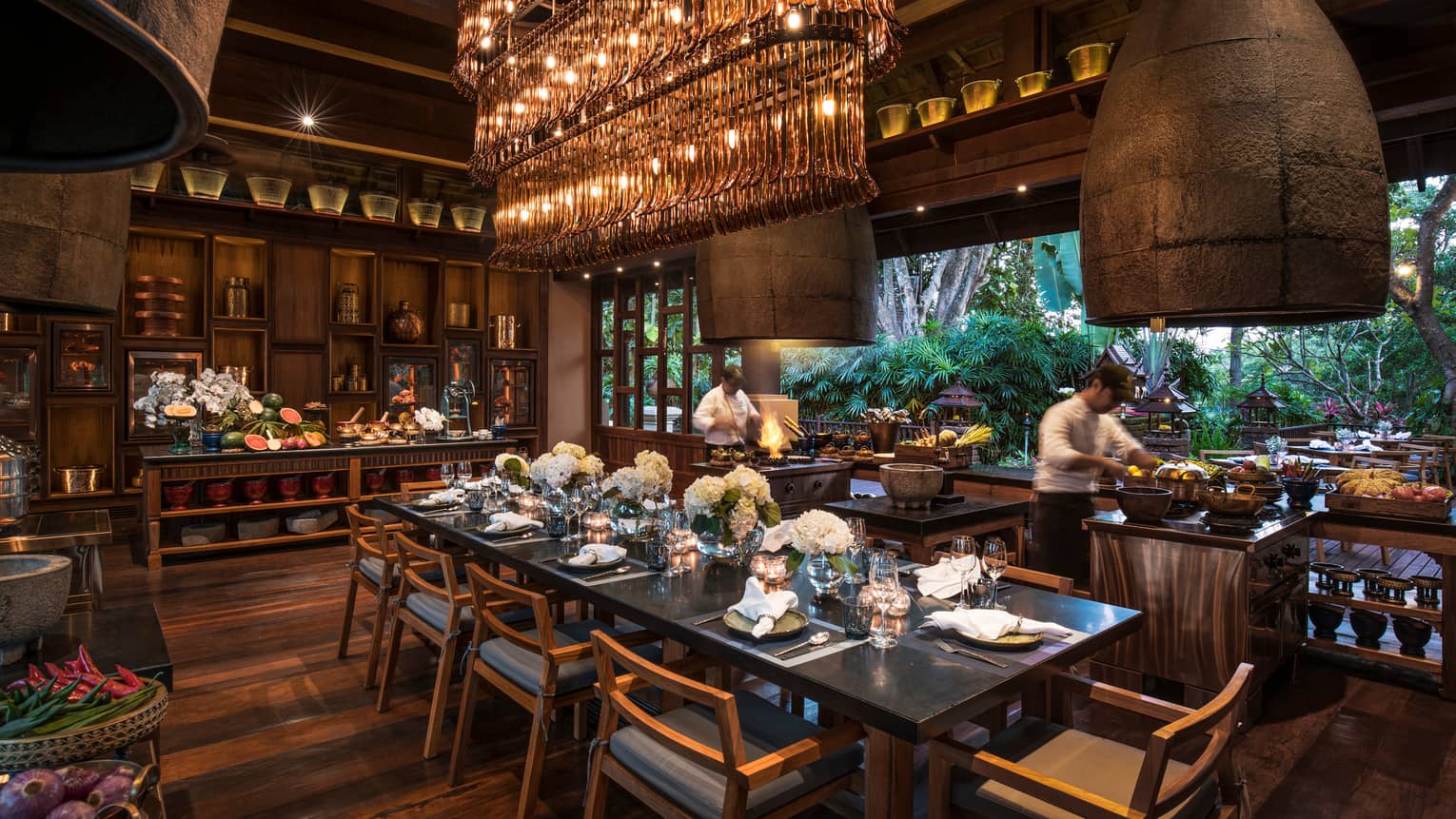 Large dining table under long rectangular crystal chandelier in Rim Tai restaurant, chefs in background