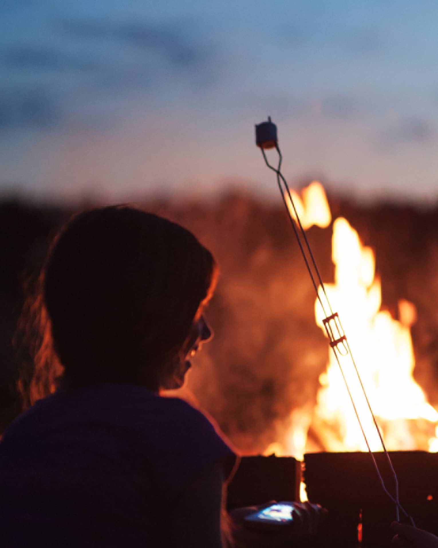 Silhouette of two children roasting marshmallows in front of roaring bonfire 