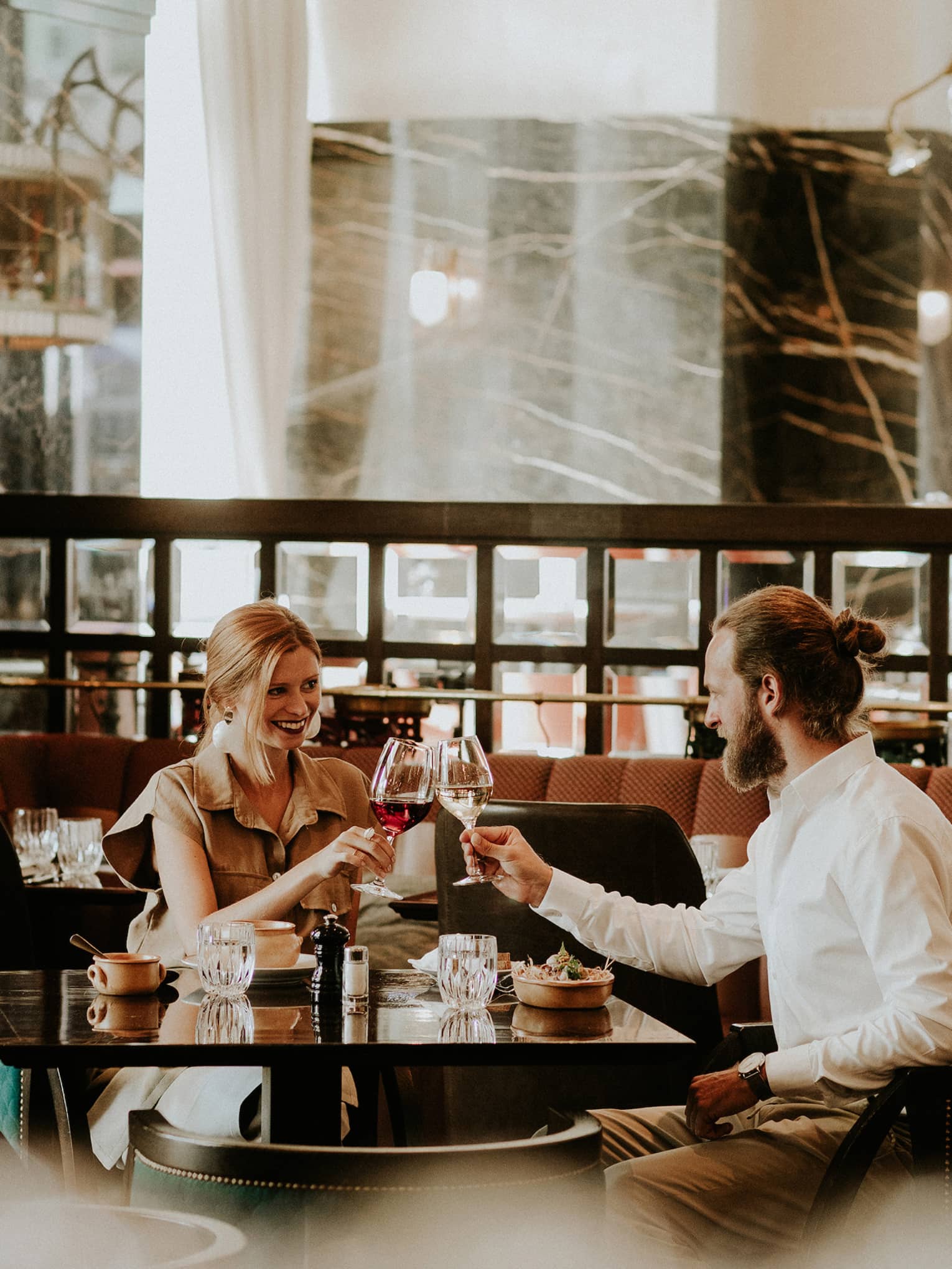 Smiling couple at table toasts with wine glasses in restaurant lounge 