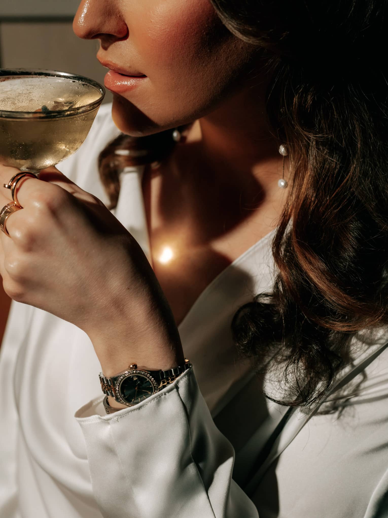 A woman with long, dark hair is about to sip a cocktail from a coupe glass.