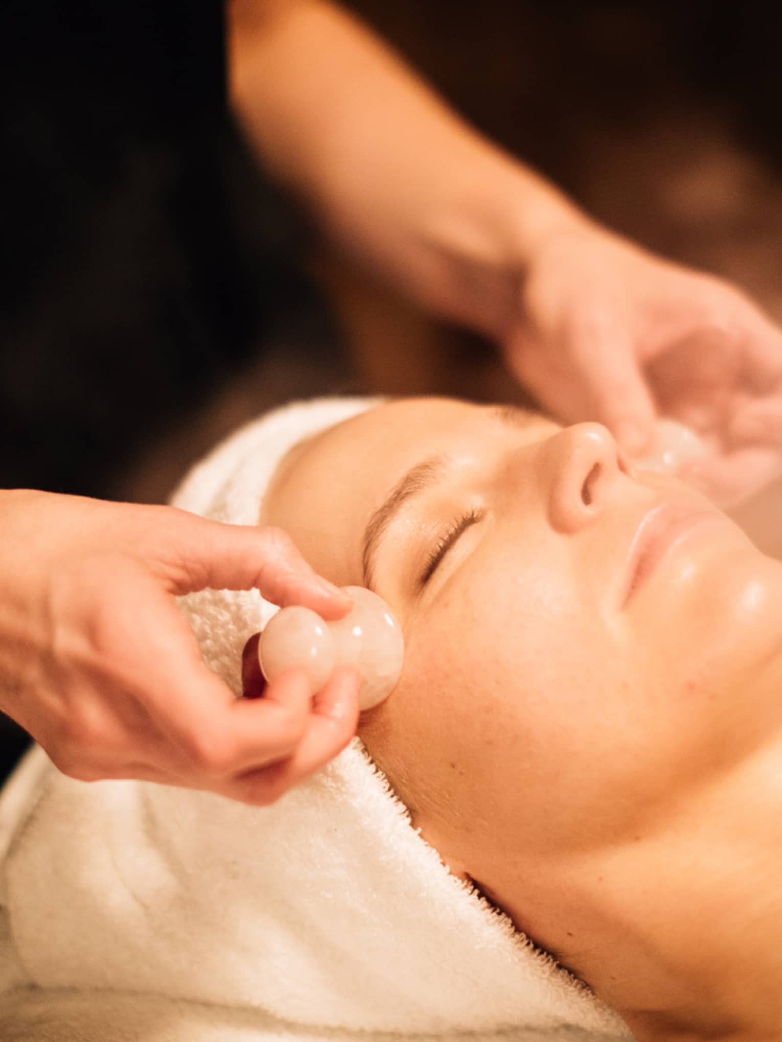 A woman receiving a facial massage with round stones.