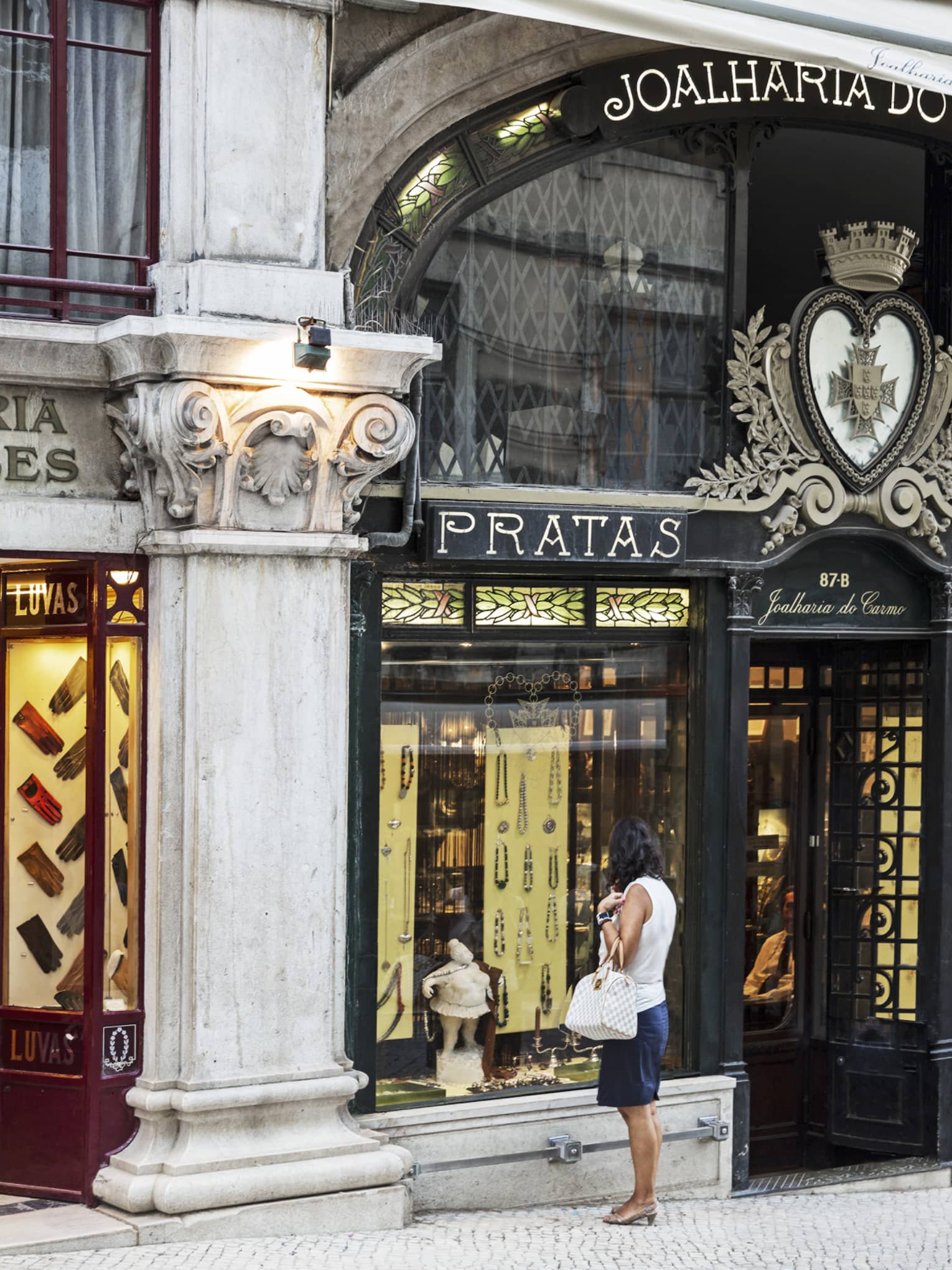 Back of woman holding white designer purse and looking into Pratas retail store window in shopping district