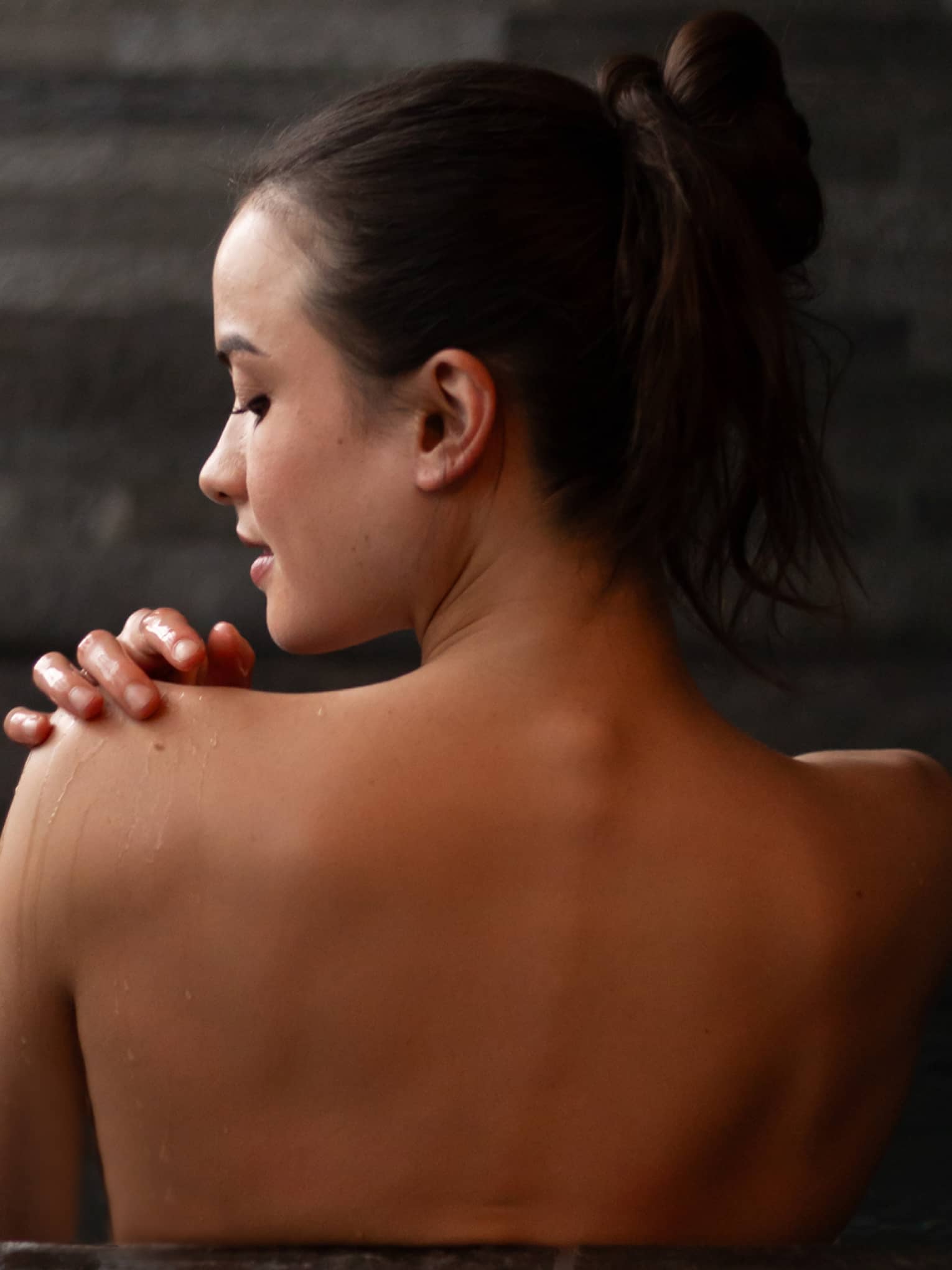 Woman with bare back to camera relaxes in a spa bath