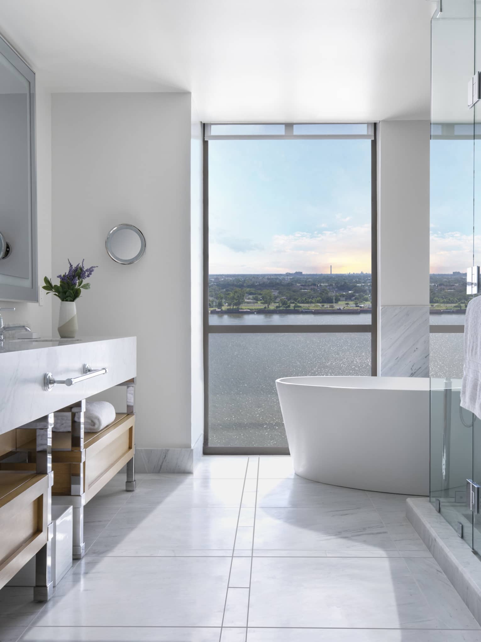 Guest room bathroom with marbled double vanity, full-width mirror, large soaking tub, floor-to-ceiling window