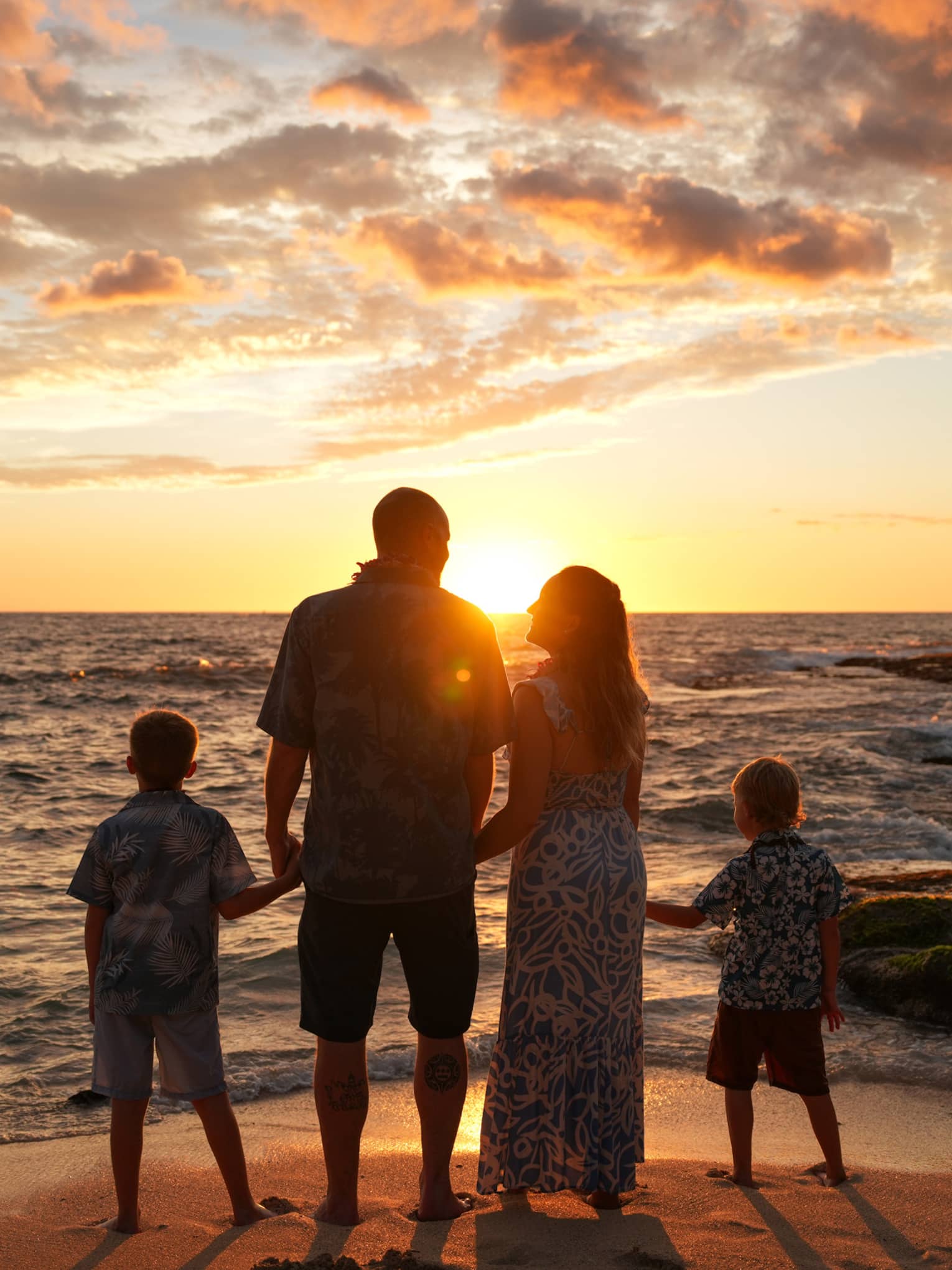 A family of four poses on a beach at sunset, facing away from the camera