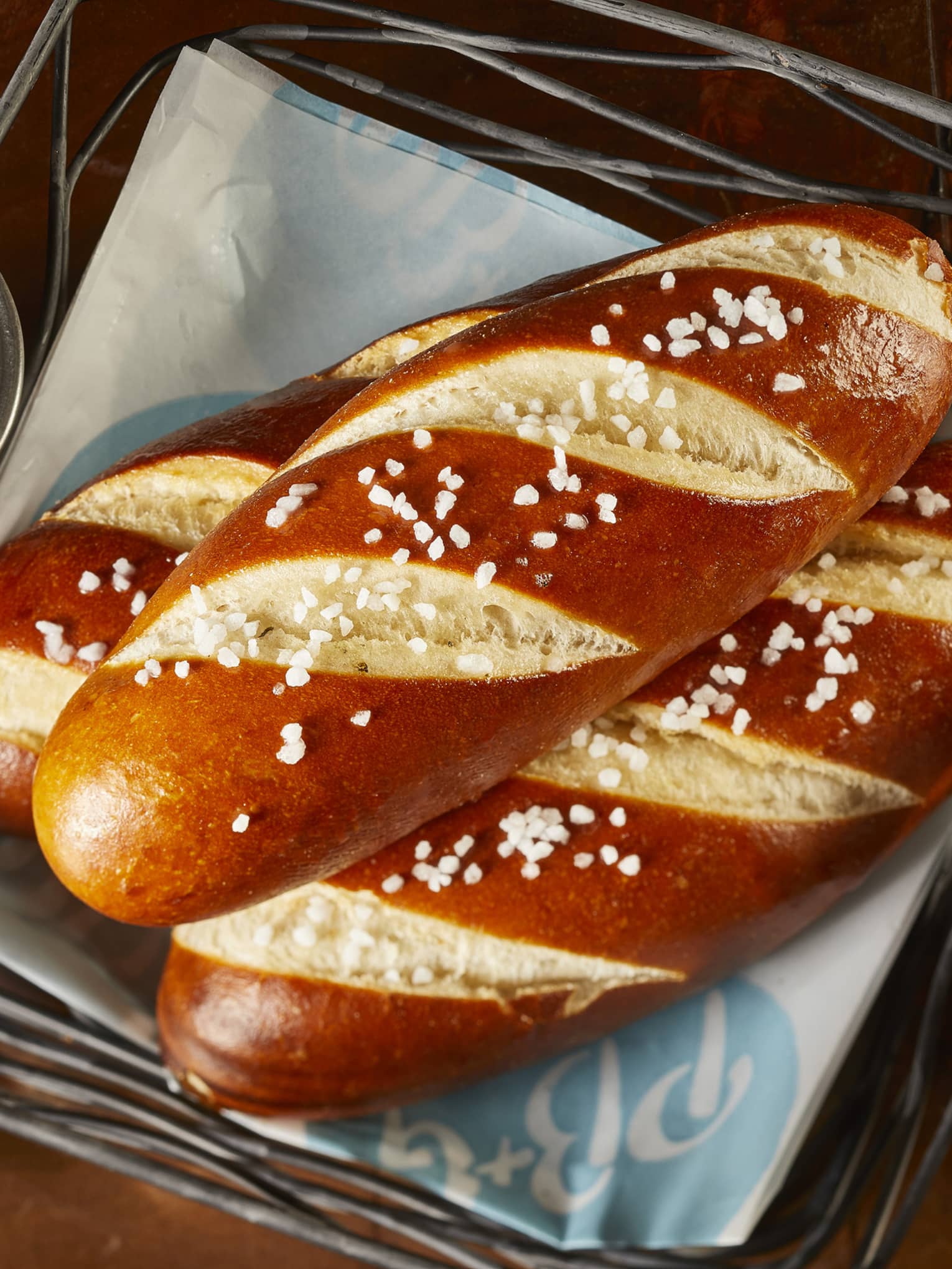 Three large pretzels in a basket with a white and brown sauce in small cups.