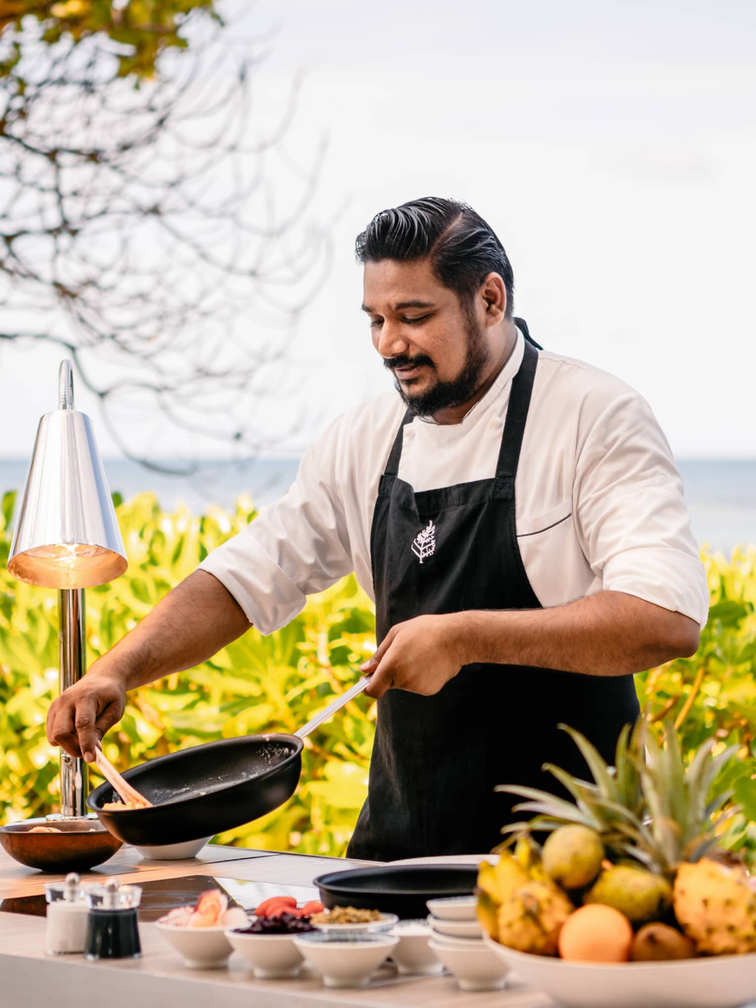 Chef in black apron at outdoor prep area cooking brunch dishes