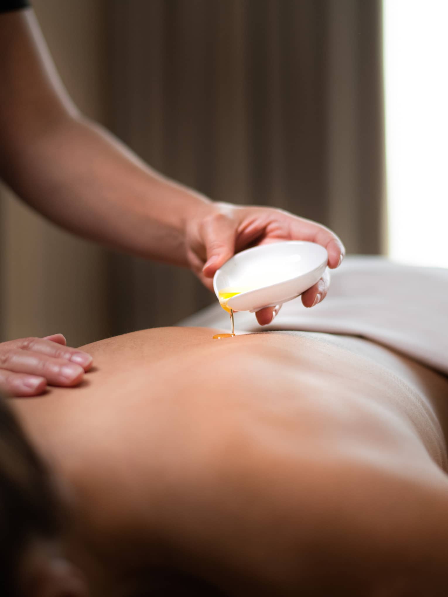 Spa staff pours hot oil on person's back during massage