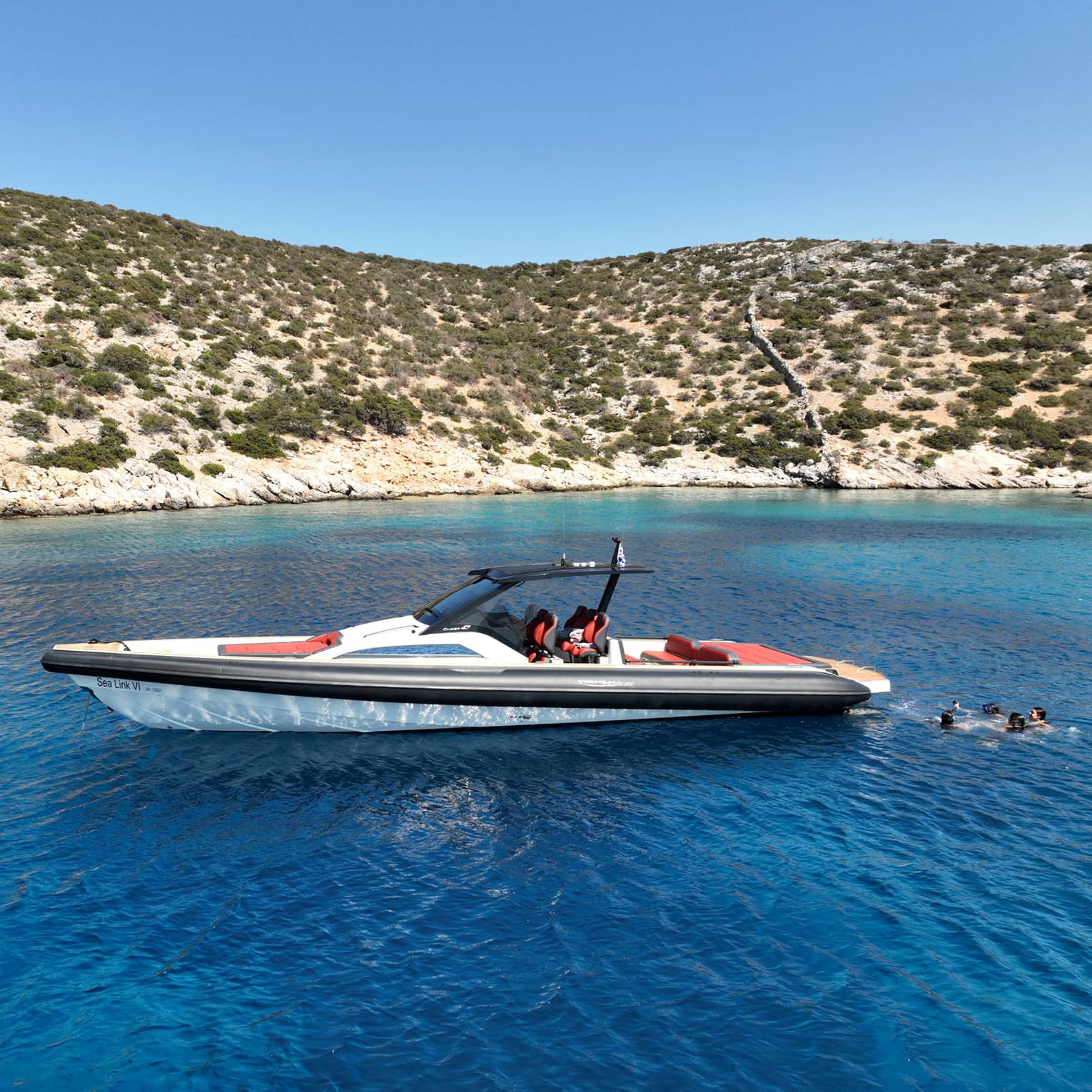 People swim behind a luxury boat in the blue waters close to the coast.