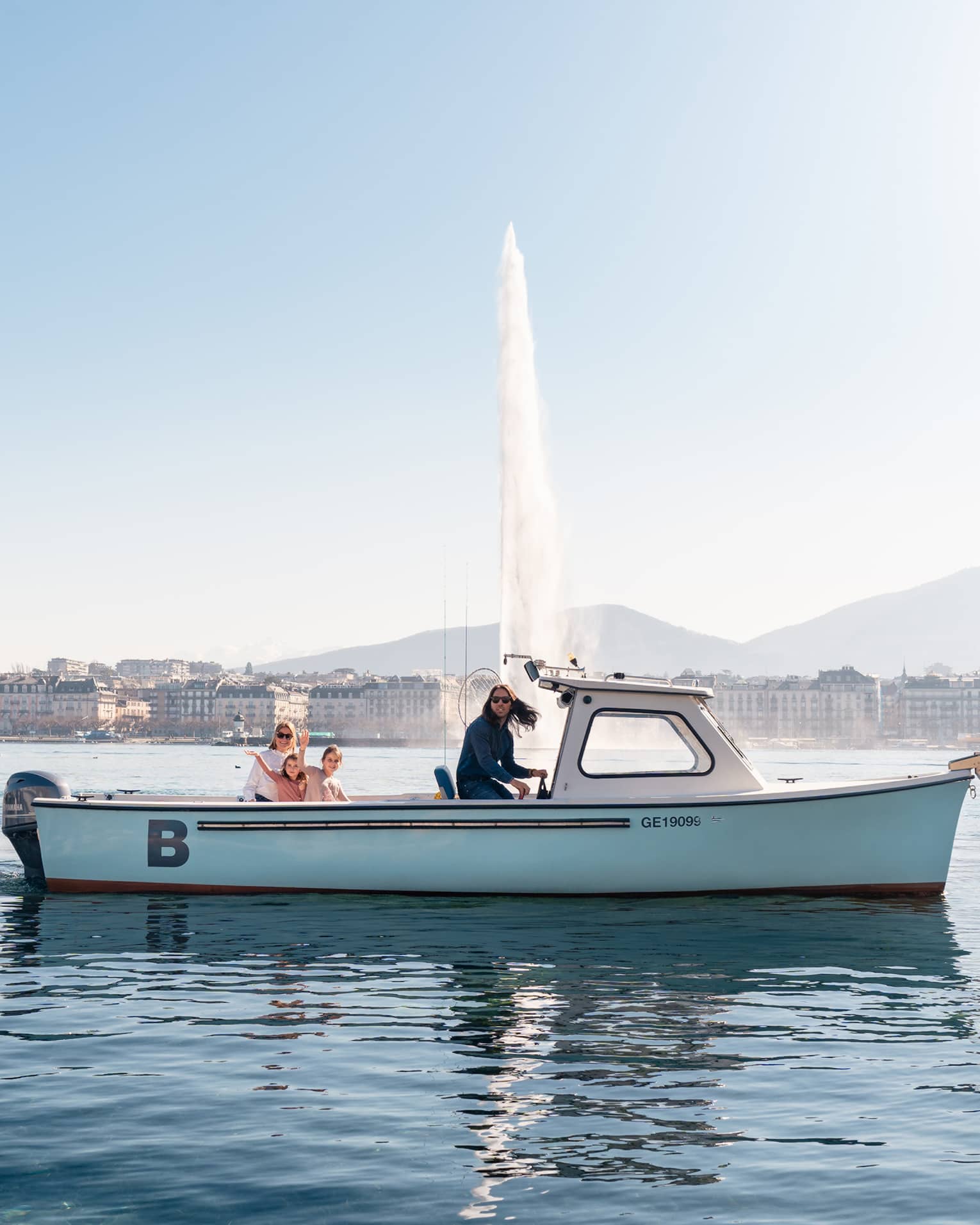 Four people in small boat on Lake Geneva with Jet d'Eau fountain and city in backdrop