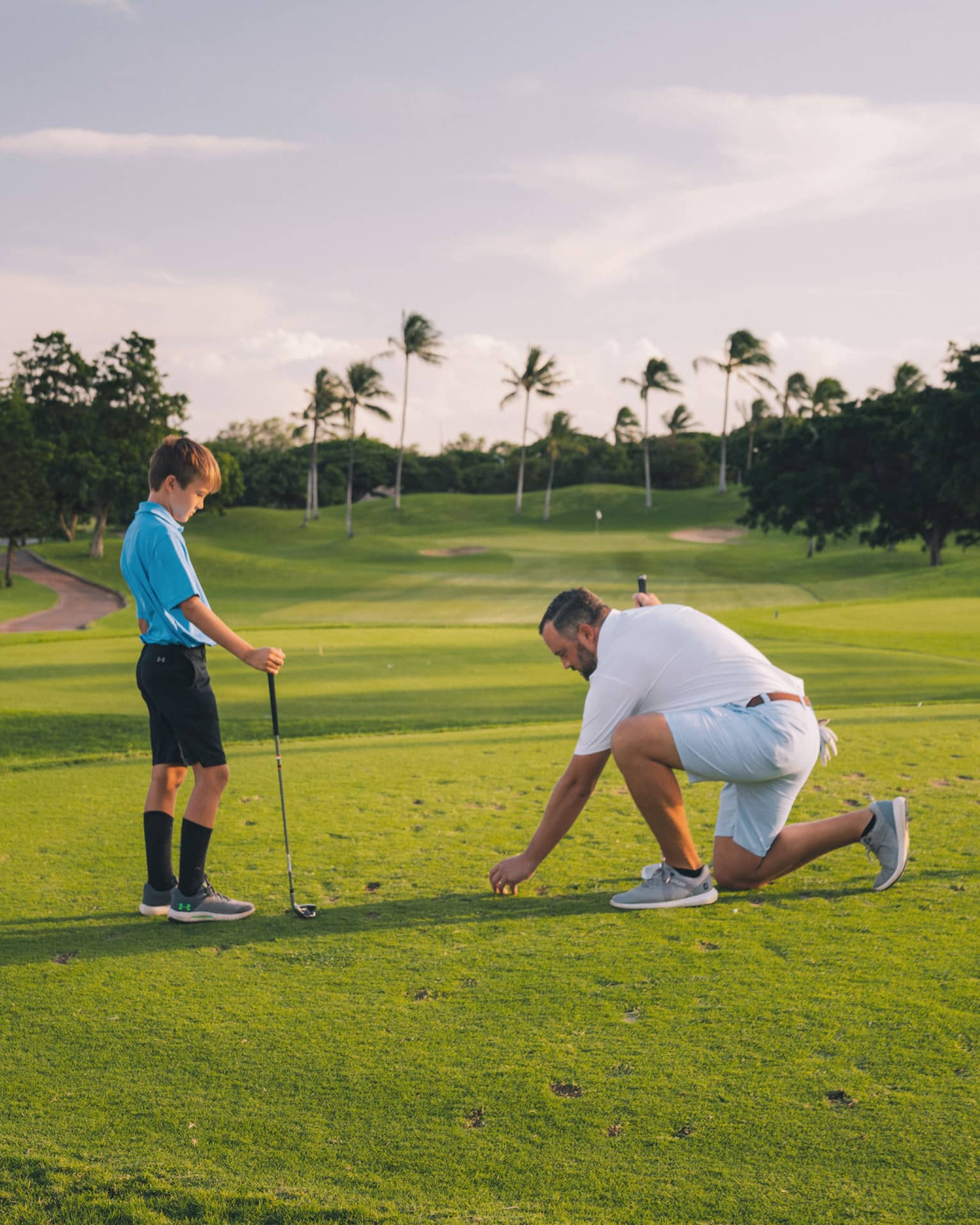 Man and young son play golf on the green, blue sky and palm trees in background 