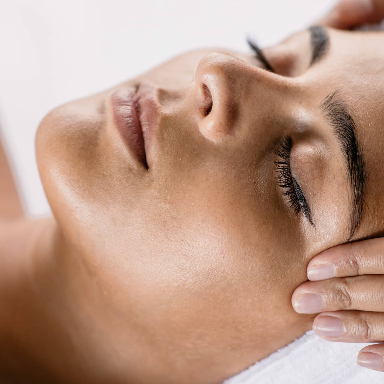 Hands massage woman's temples as she closes her eyes, spa towel around hair