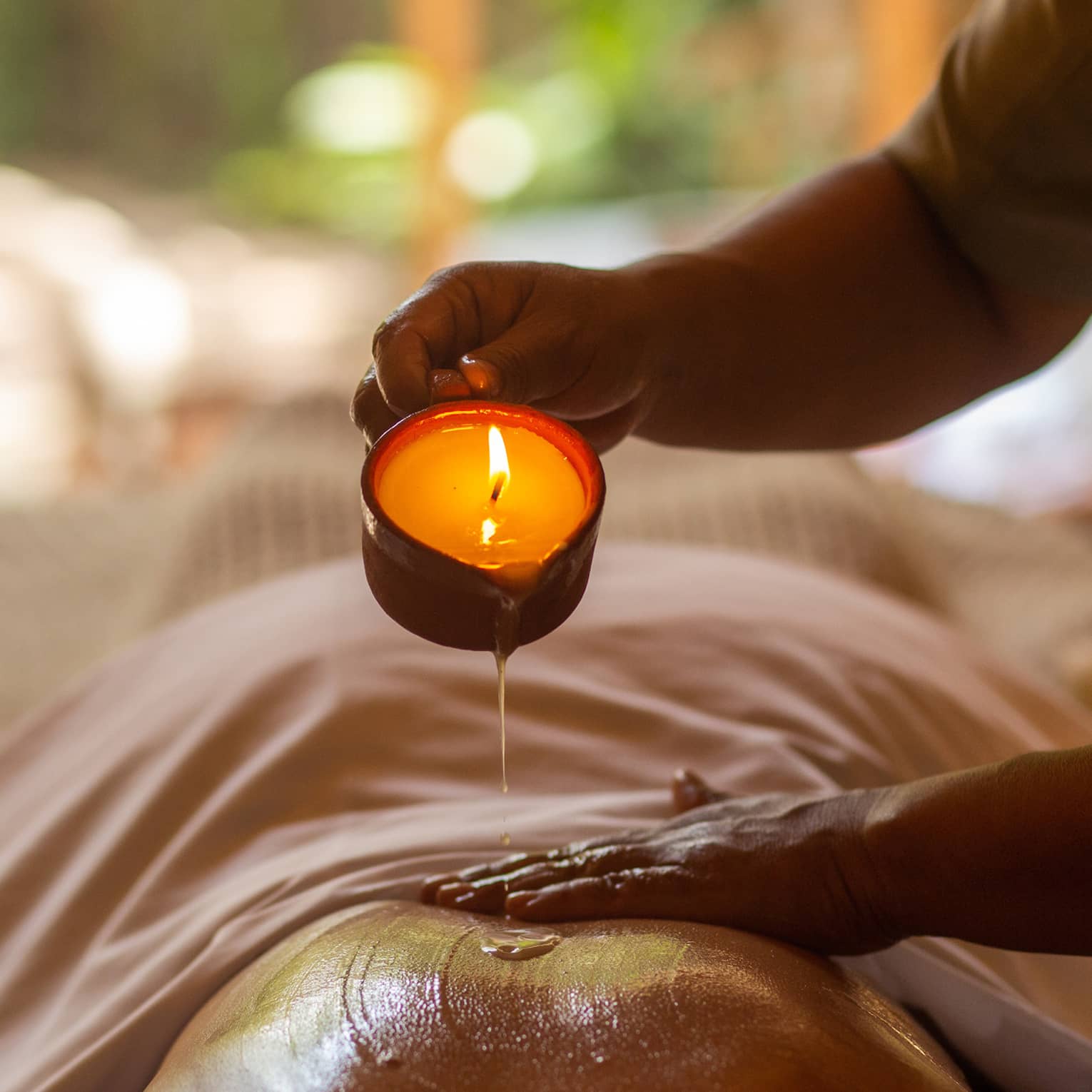 Massage therapist pours hot wax from candle onto bare back of guest