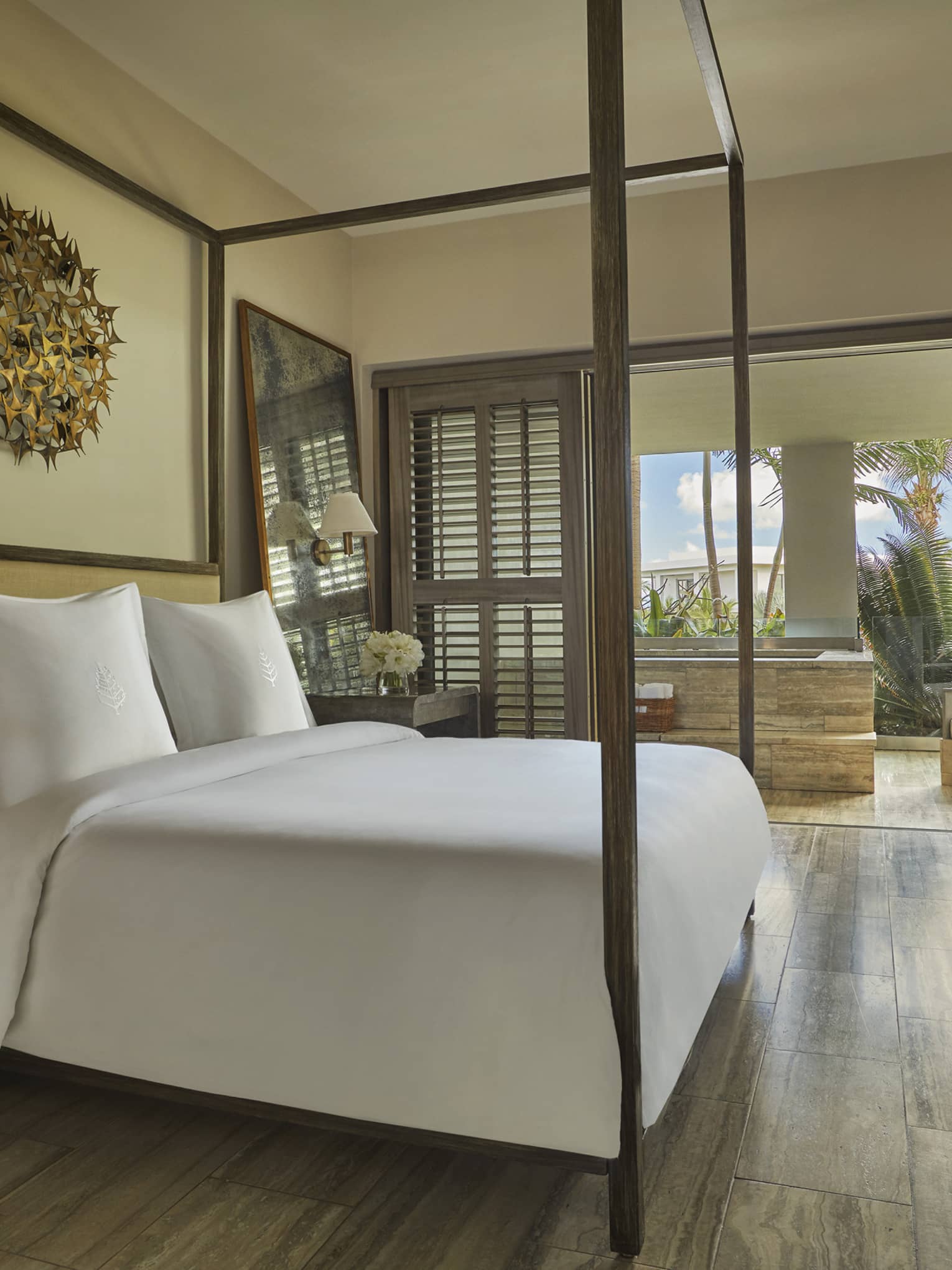 Elegant bedroom with canopy bed, wooden floors and a terrace view of palm trees and blue sky