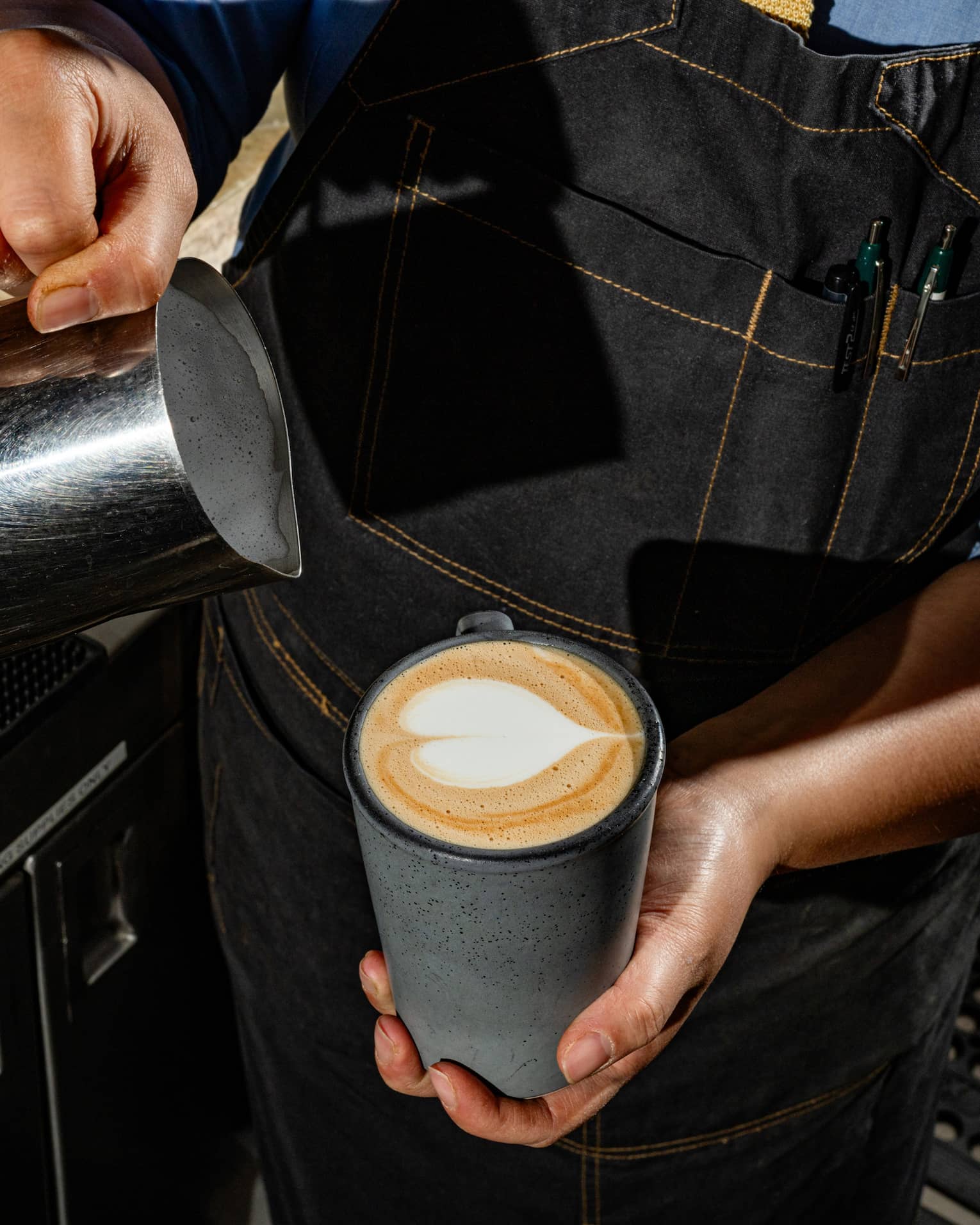 A person pouring milk in a mug of coffee