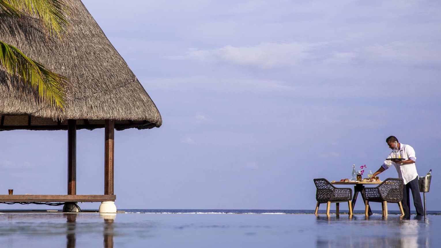 Hotel staff sets patio table at edge of infinity outdoor swimming pool