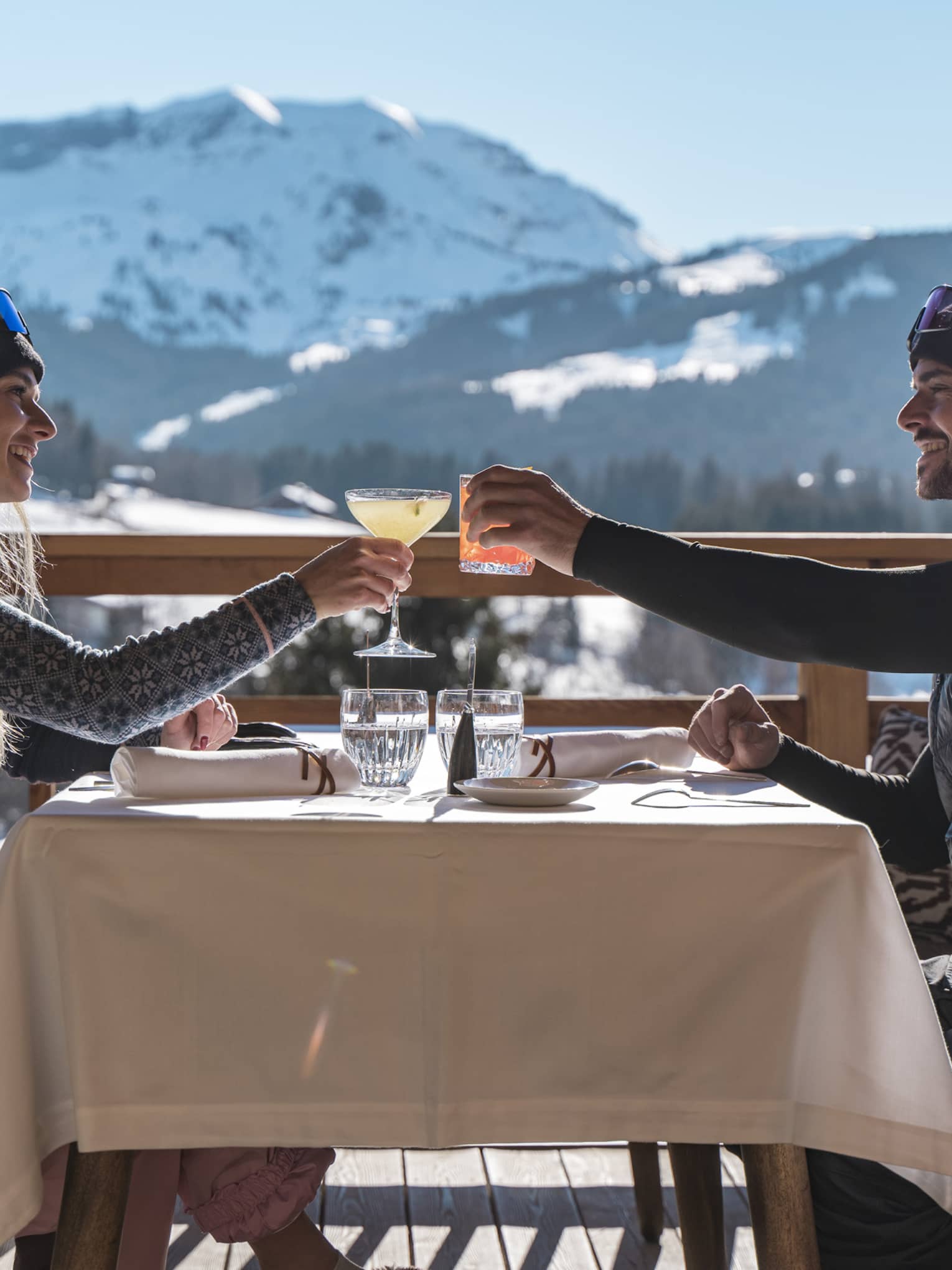 Two people drinking on a patio outside with snowy mountains in the distance
