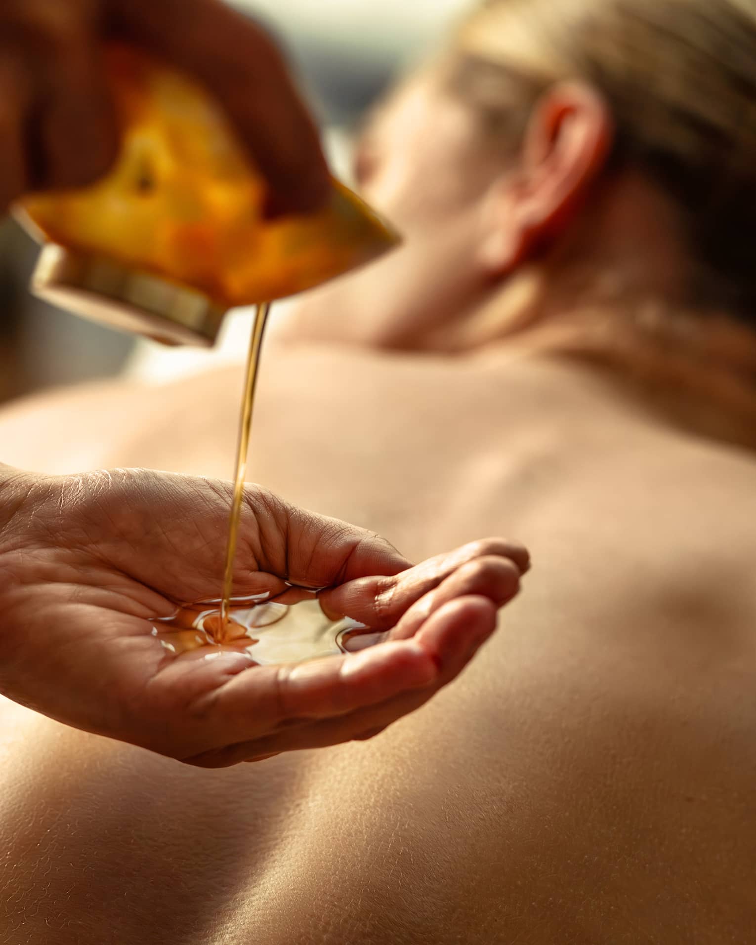 Person pouring oil into their hands while other person lies on spa table.