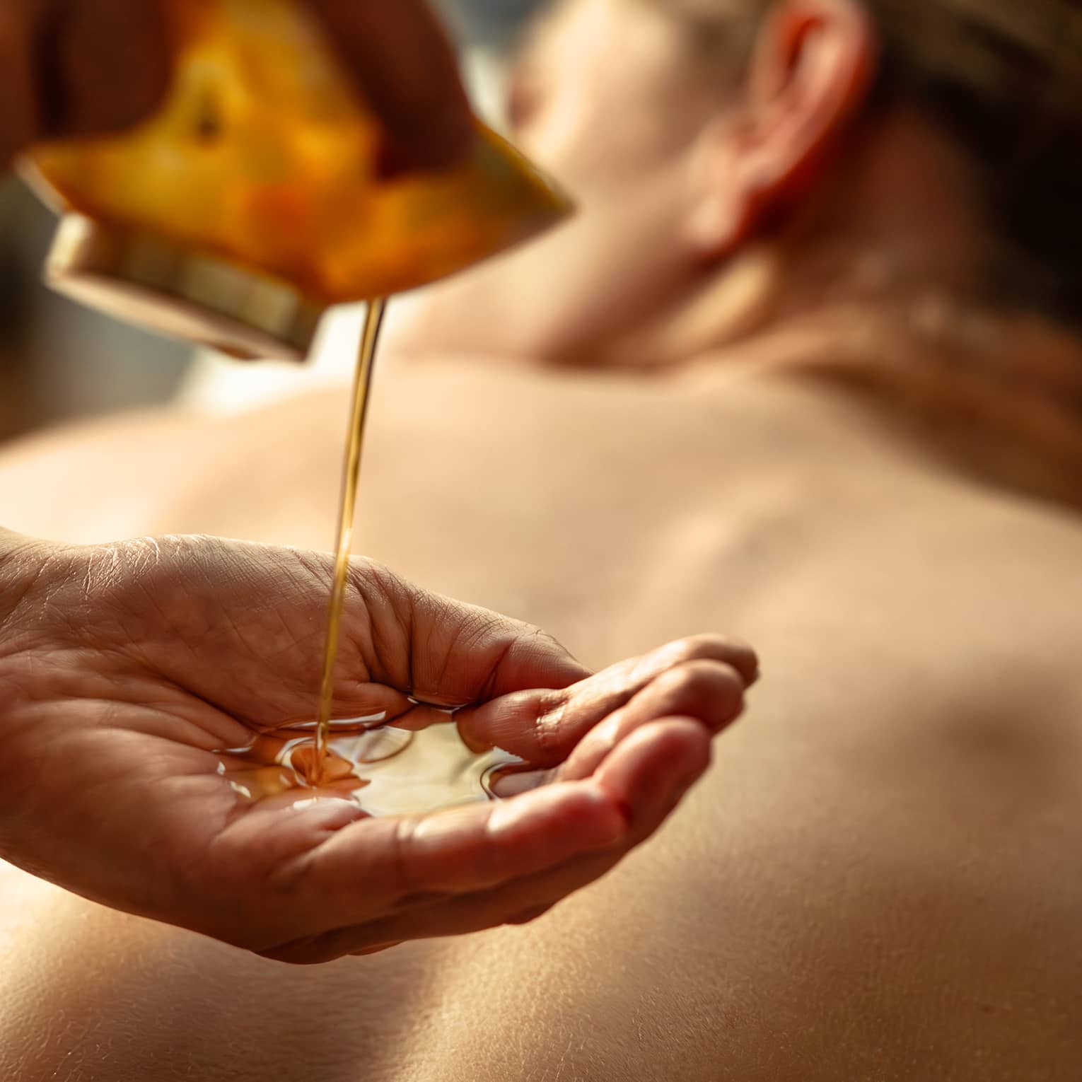 Person pouring oil into their hands while other person lies on spa table.