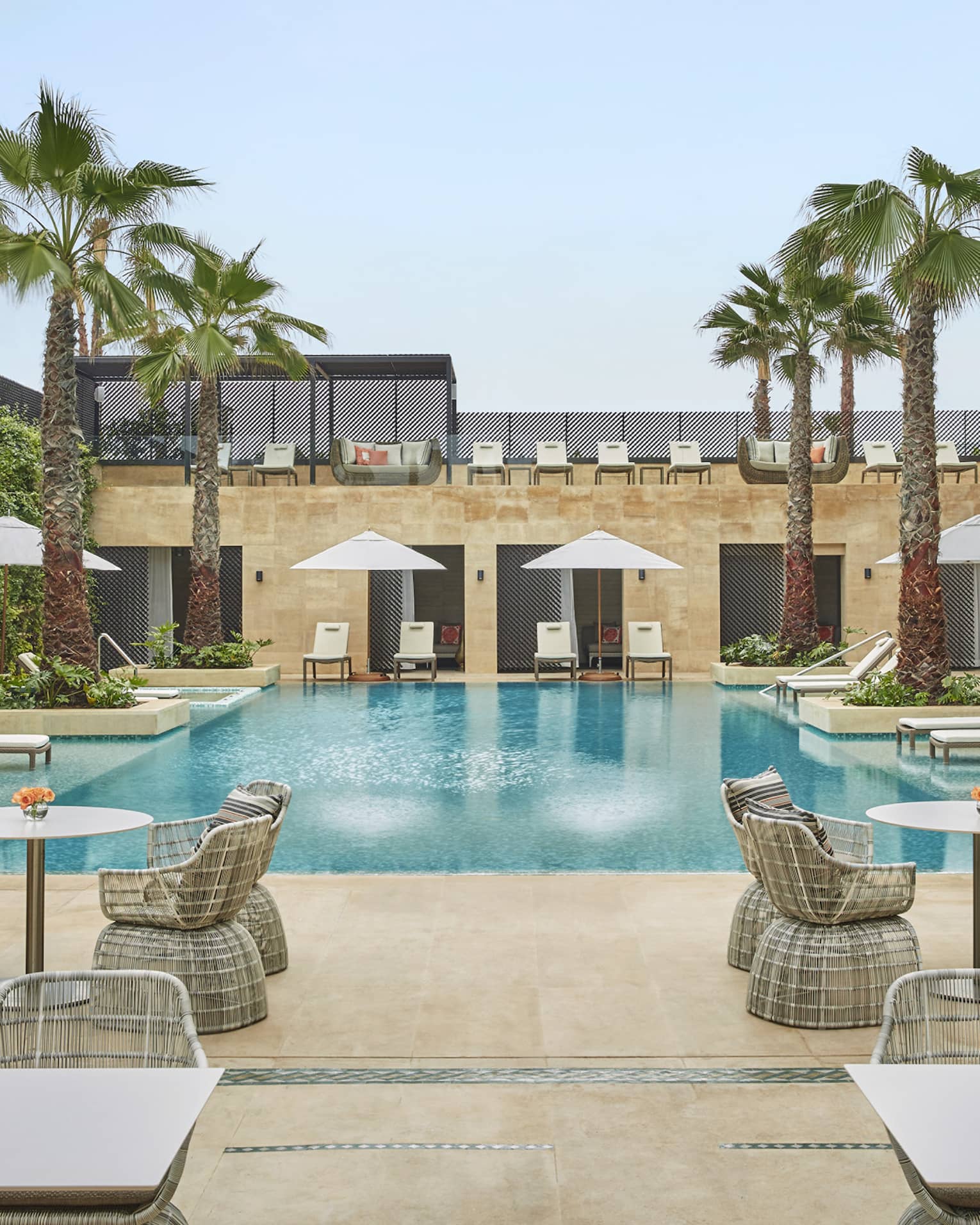 Courtyard pool flanked by tables and chairs with umbrellas, palm trees