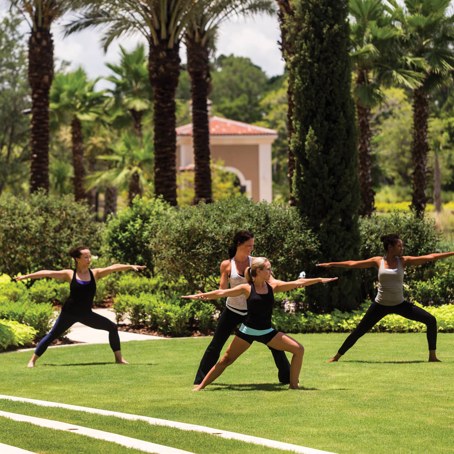 Group of people stand, arms outstretched in yoga poses on green lawn