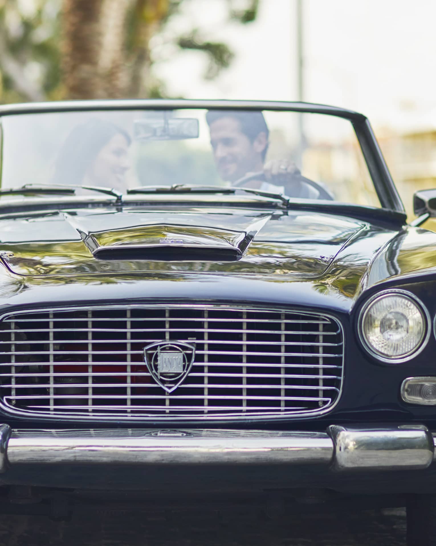Man and woman sit in black vintage car smiling 