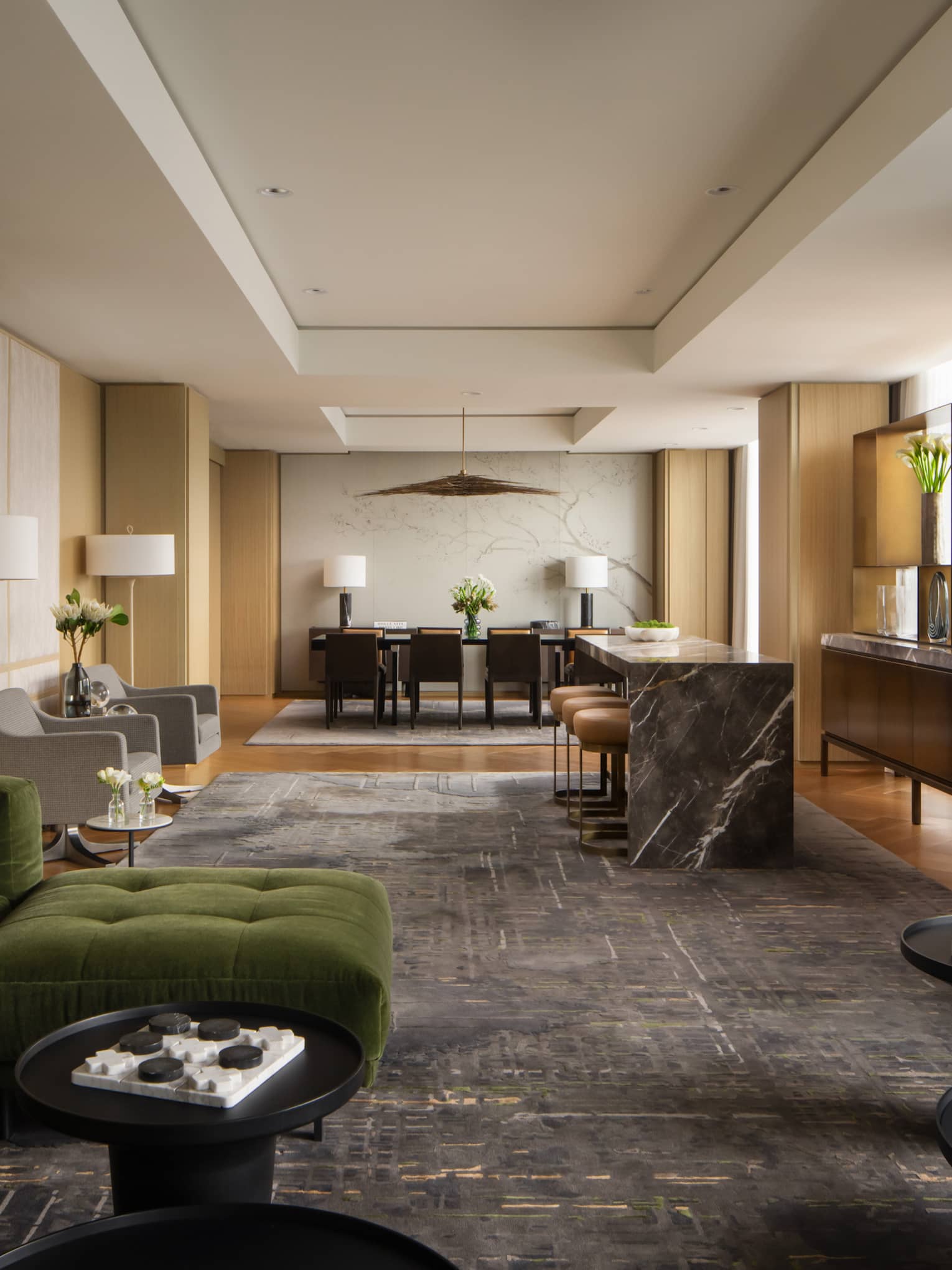 Luxury hotel suite lounge area with a green velvet sectional, marble-top bar, modern dining table, and open shelving with decorative accents
