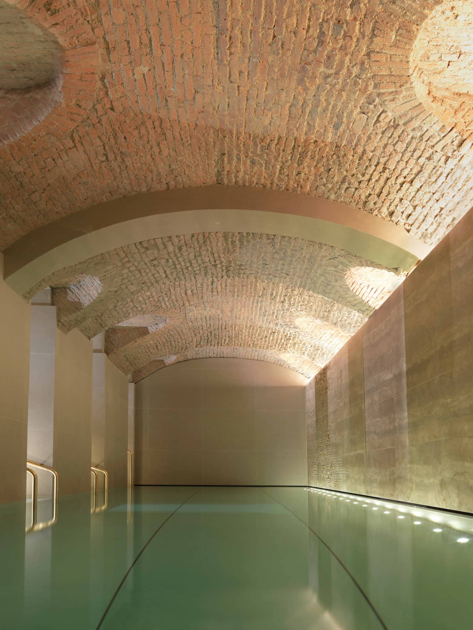Indoor lap swimming pool with gold railings under curved stone ceiling