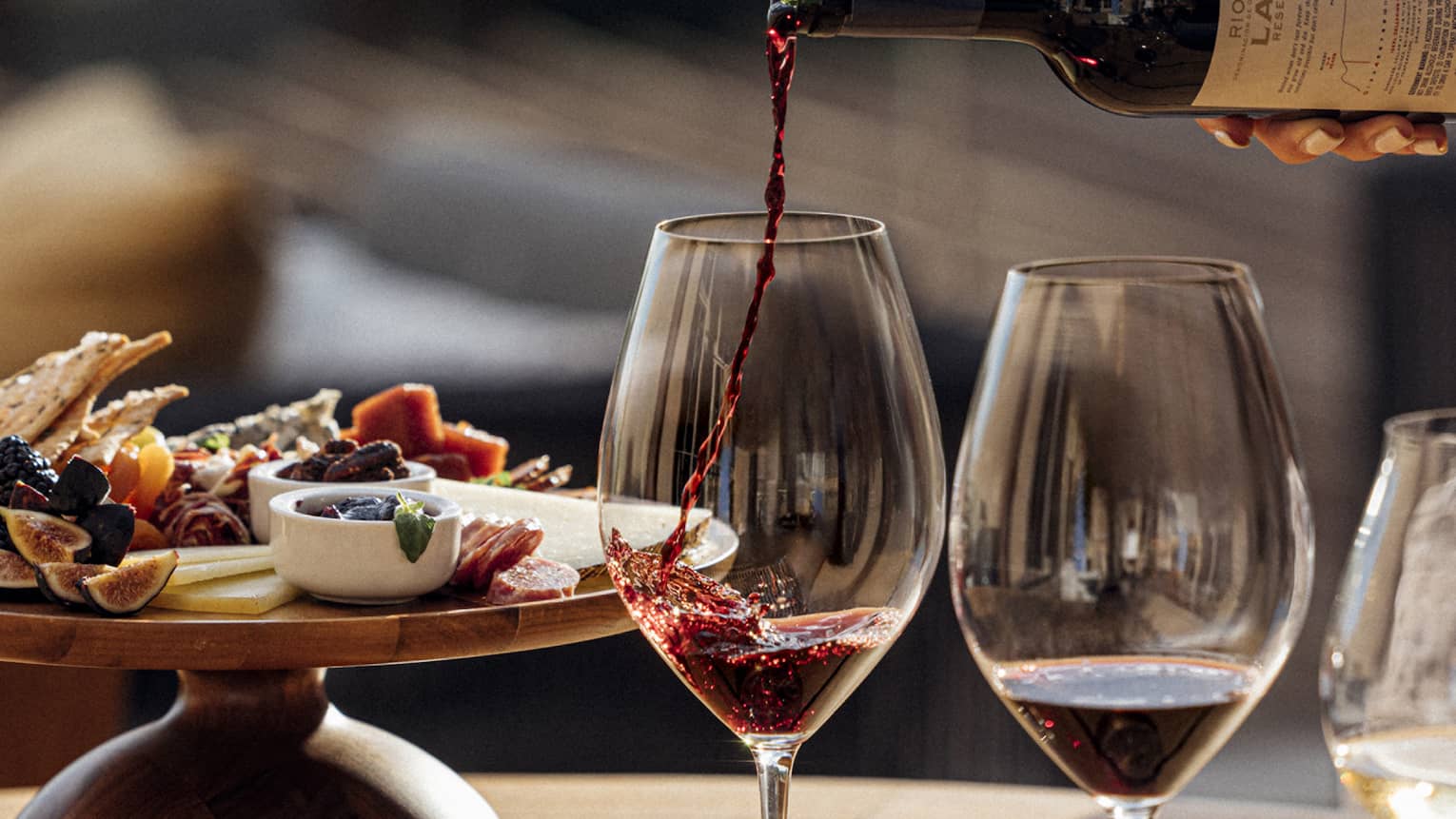 Three glasses of wine are poured next to a plate of charcuterie