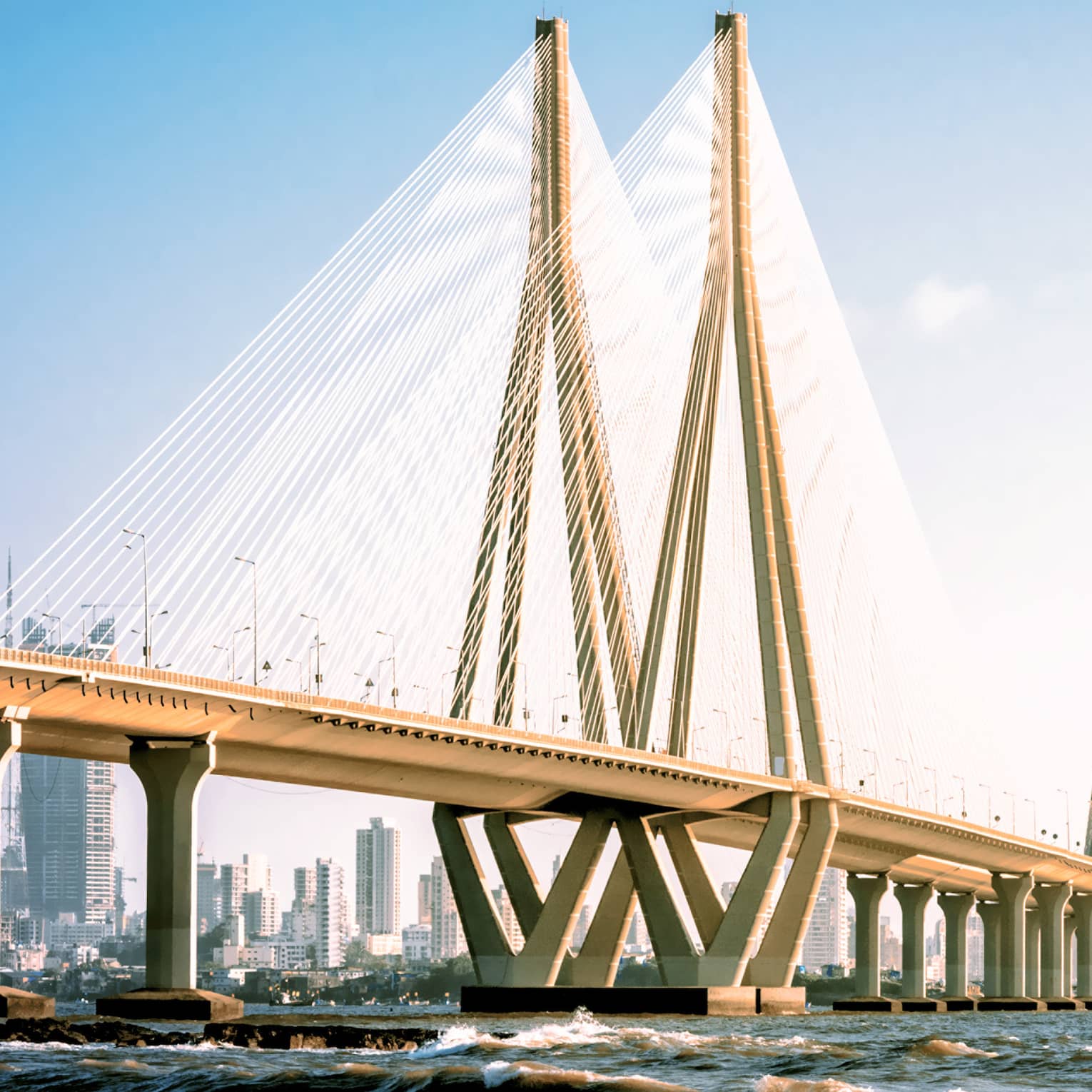 View from the water of a kilometres-long bridge featuring a triangular tower connected by scores of luminous steel cables.