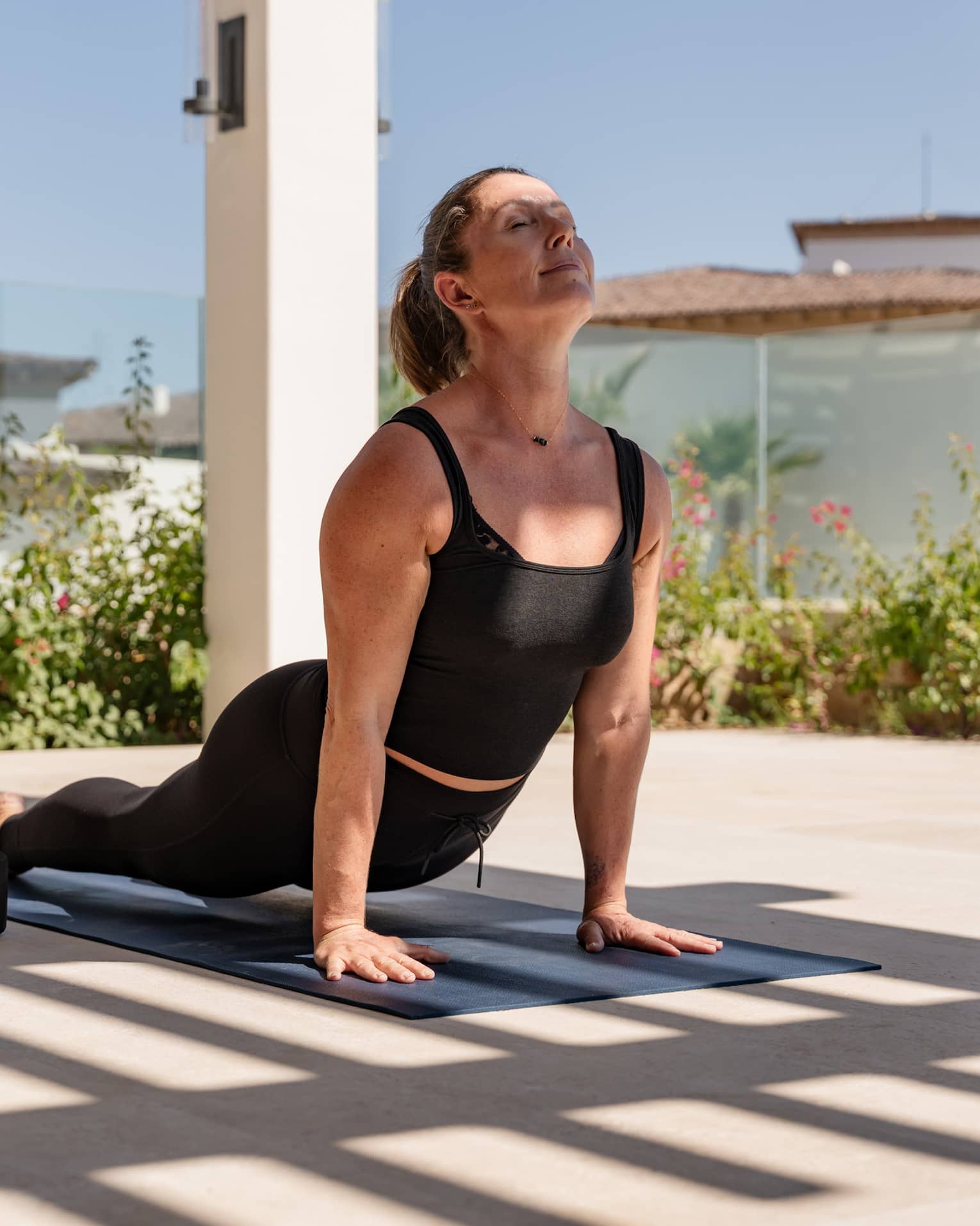 In the shade of a trellis, a guest gets a deep low back bend supported by their hands in an upward-facing-dog yoga pose.