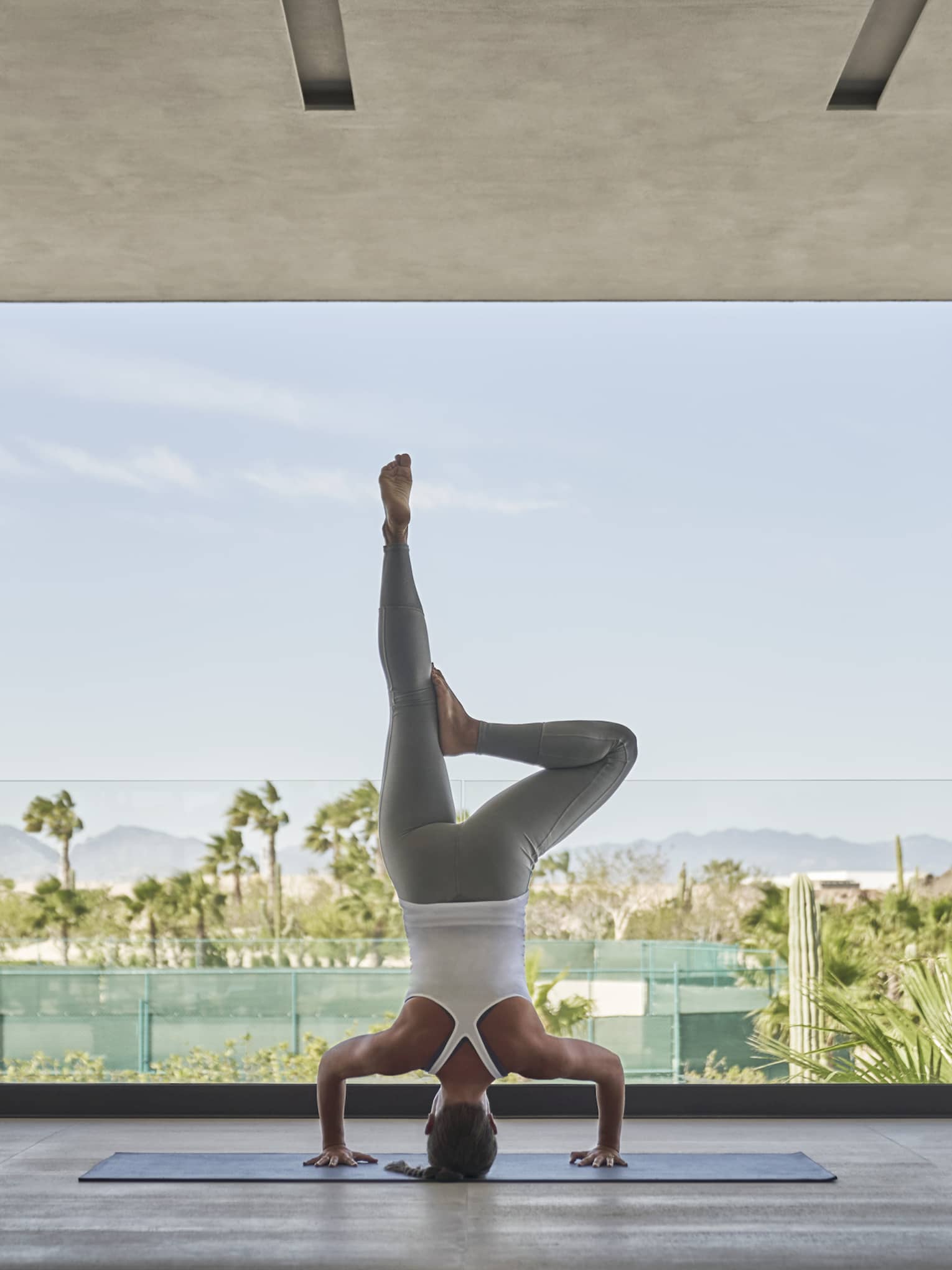 A woman doing a yoga pose while standing on her head in a large open outdoor area.