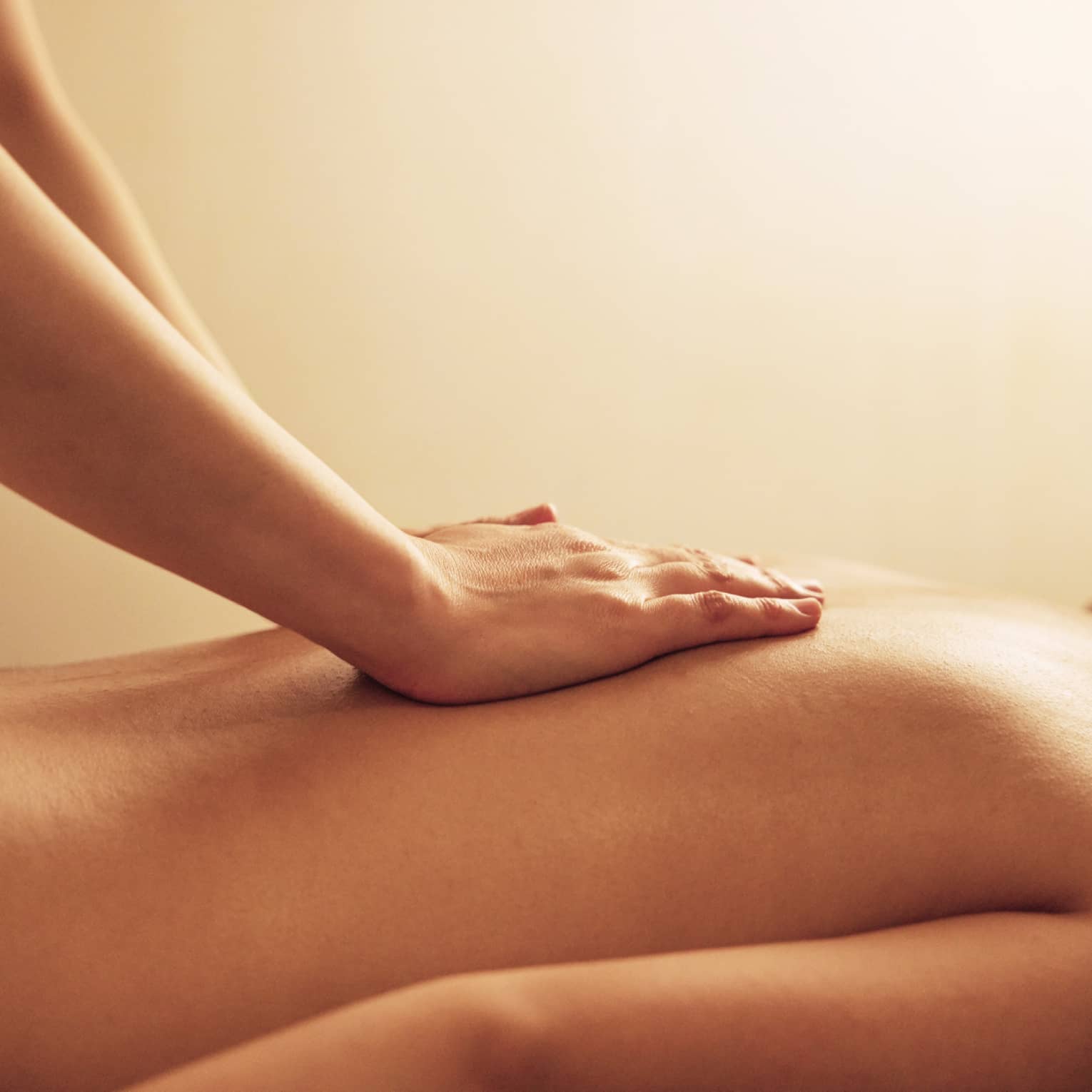 Masseuse rests hands on woman's bare back as she lays on massage table