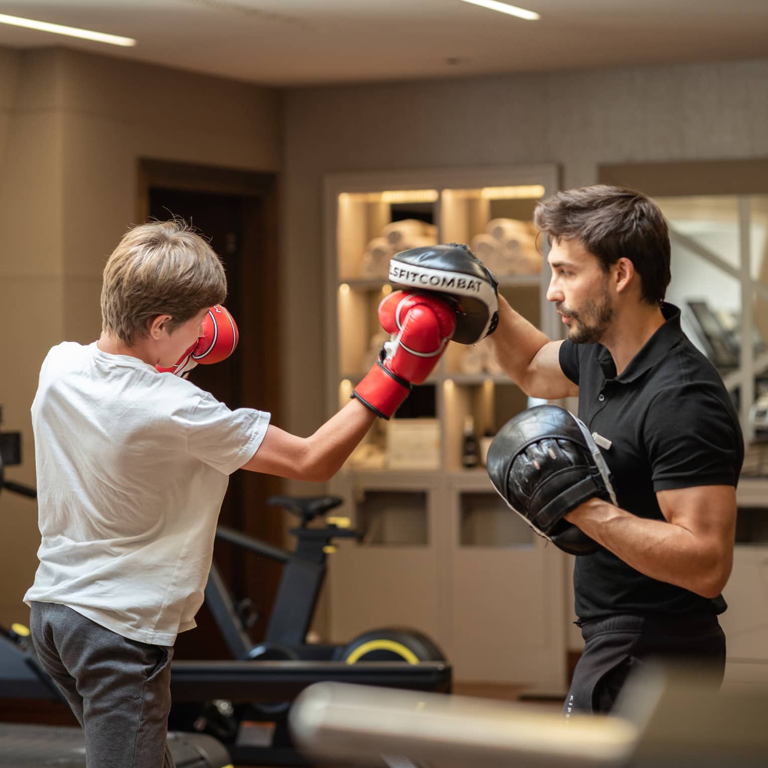 Teenager in red boxing gloves sparring with trainer in black boxing gloves in gym