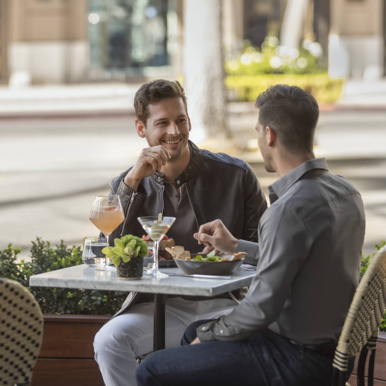Two men sitting outside eating food.
