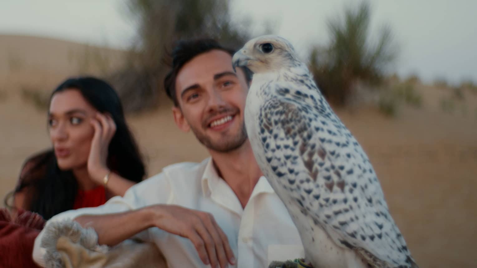 A couple sit next to an Arabian Oryx in the desert.