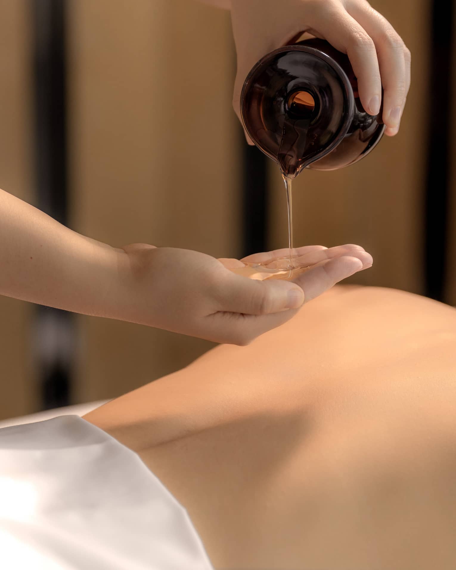 Spa therapist pours oil into hand above woman?s bare back in preparation for a massage
