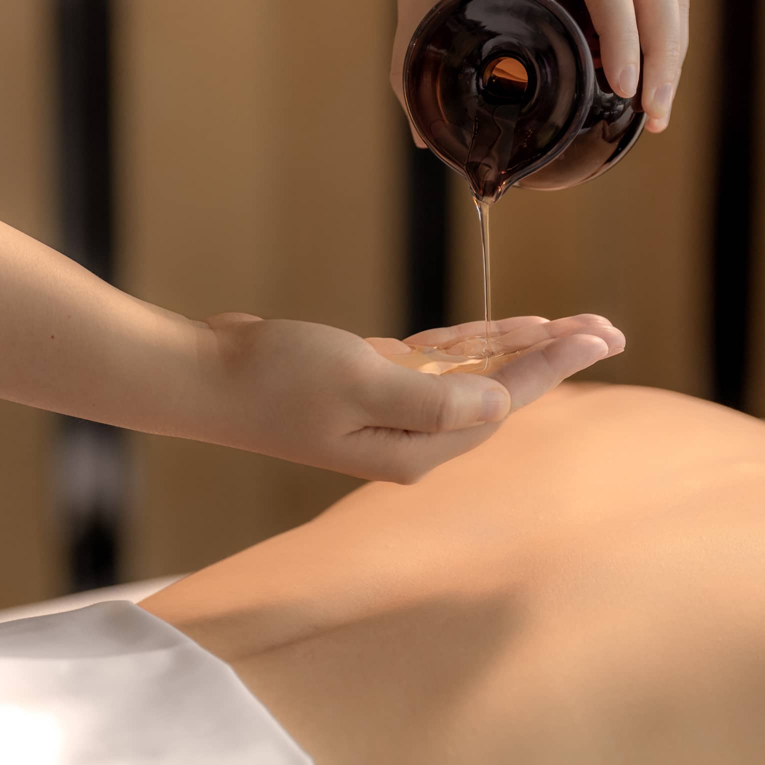 Spa therapist pours oil into hand above woman?s bare back in preparation for a massage