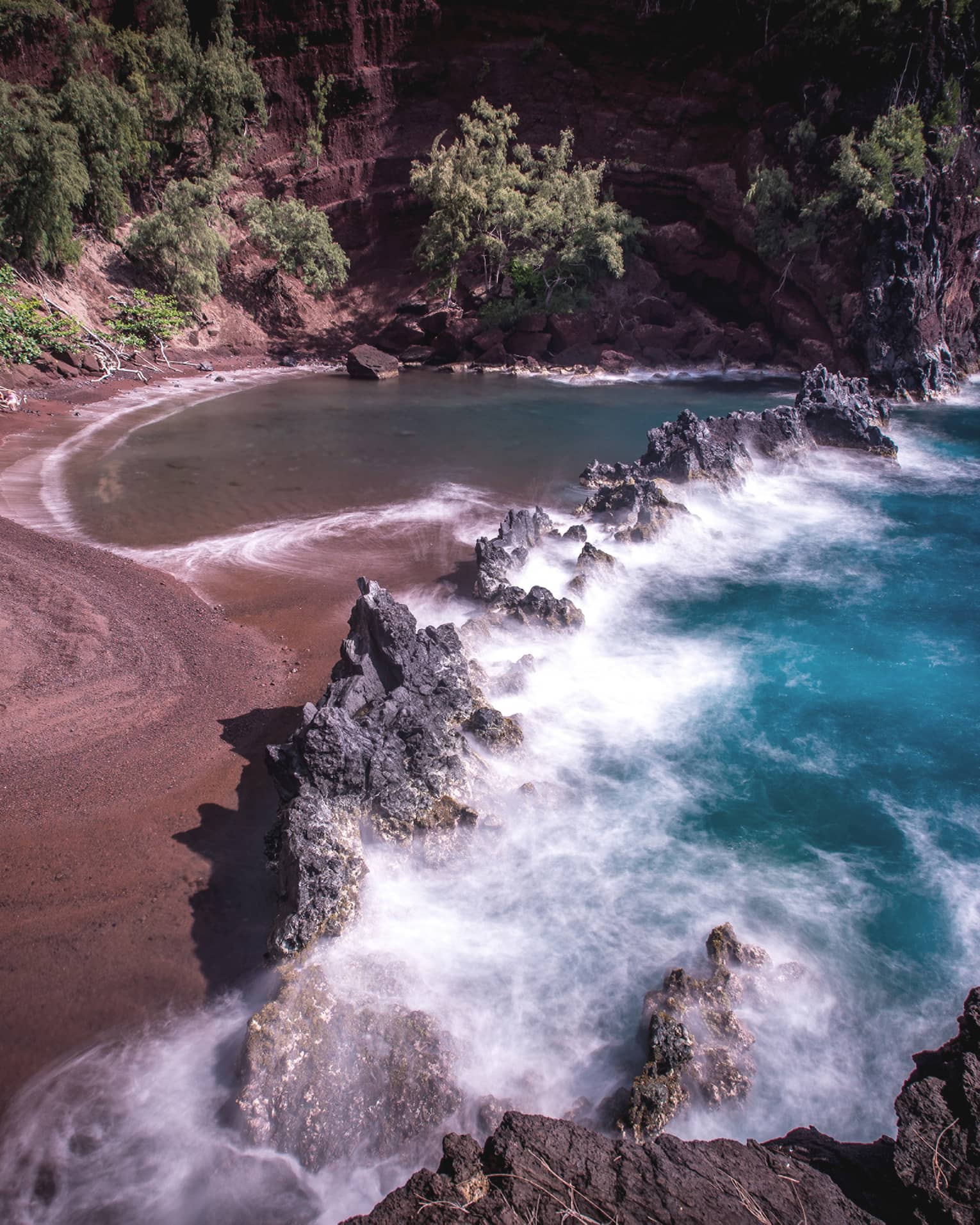 A red sand beach with waves crashing onto the sand.
