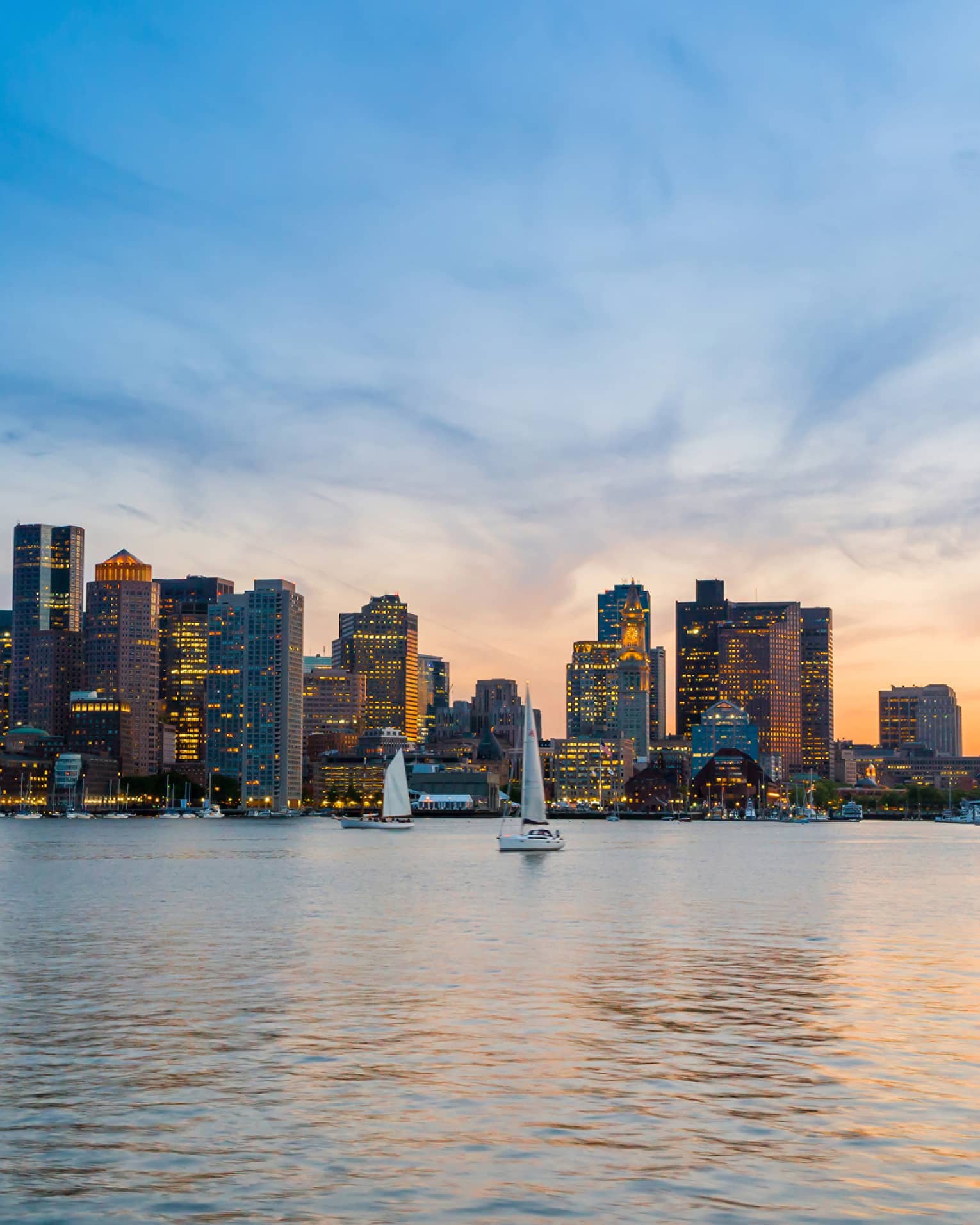 A harbour with sailboats in the water and a sunset above the city buildings