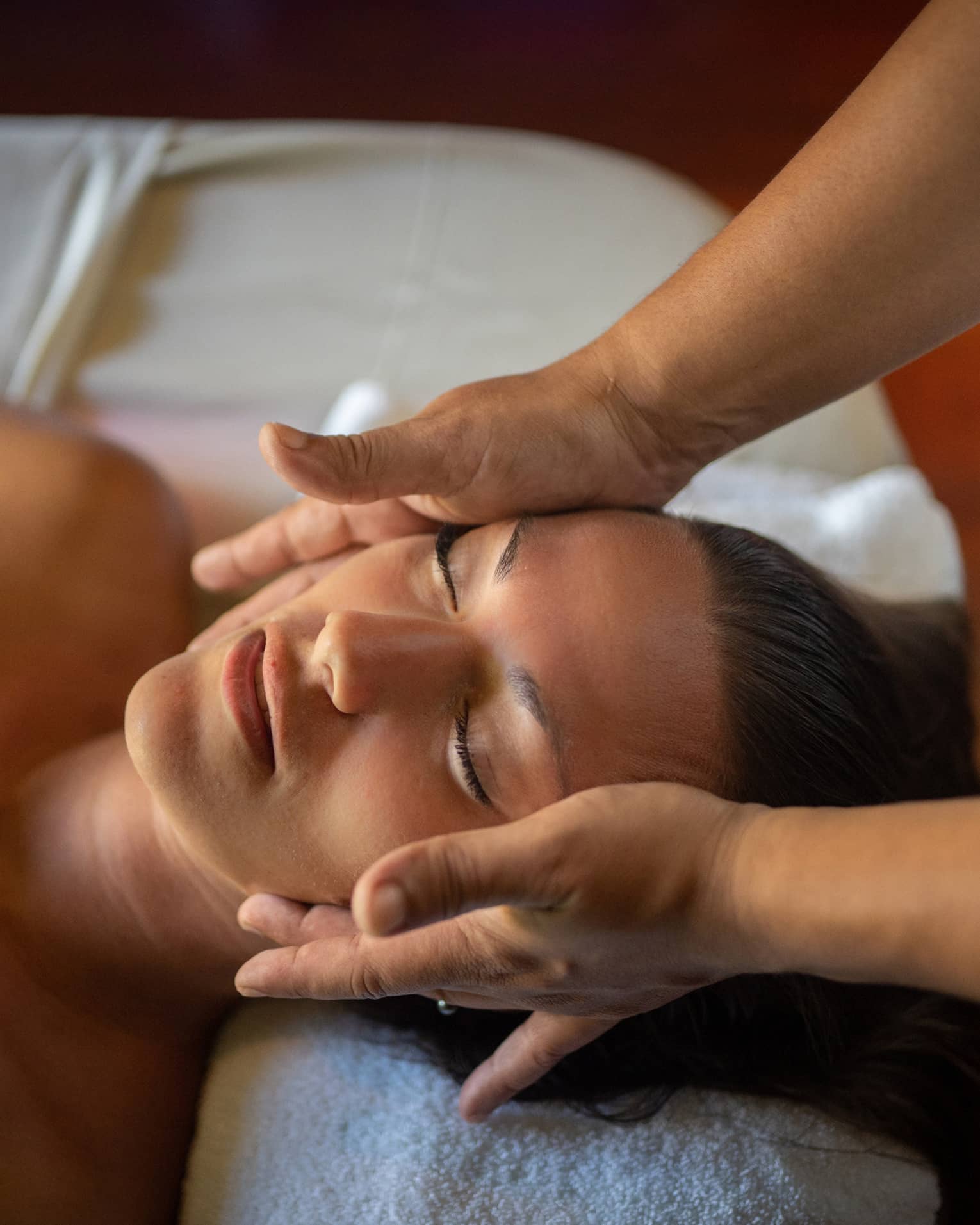 Woman lays on massage table with eyes closed as hands massage her cheeks and chin