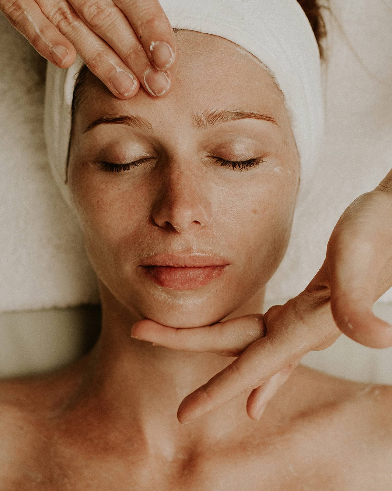 Person receiving a relaxing facial massage with eyes closed and head wrapped in a towel