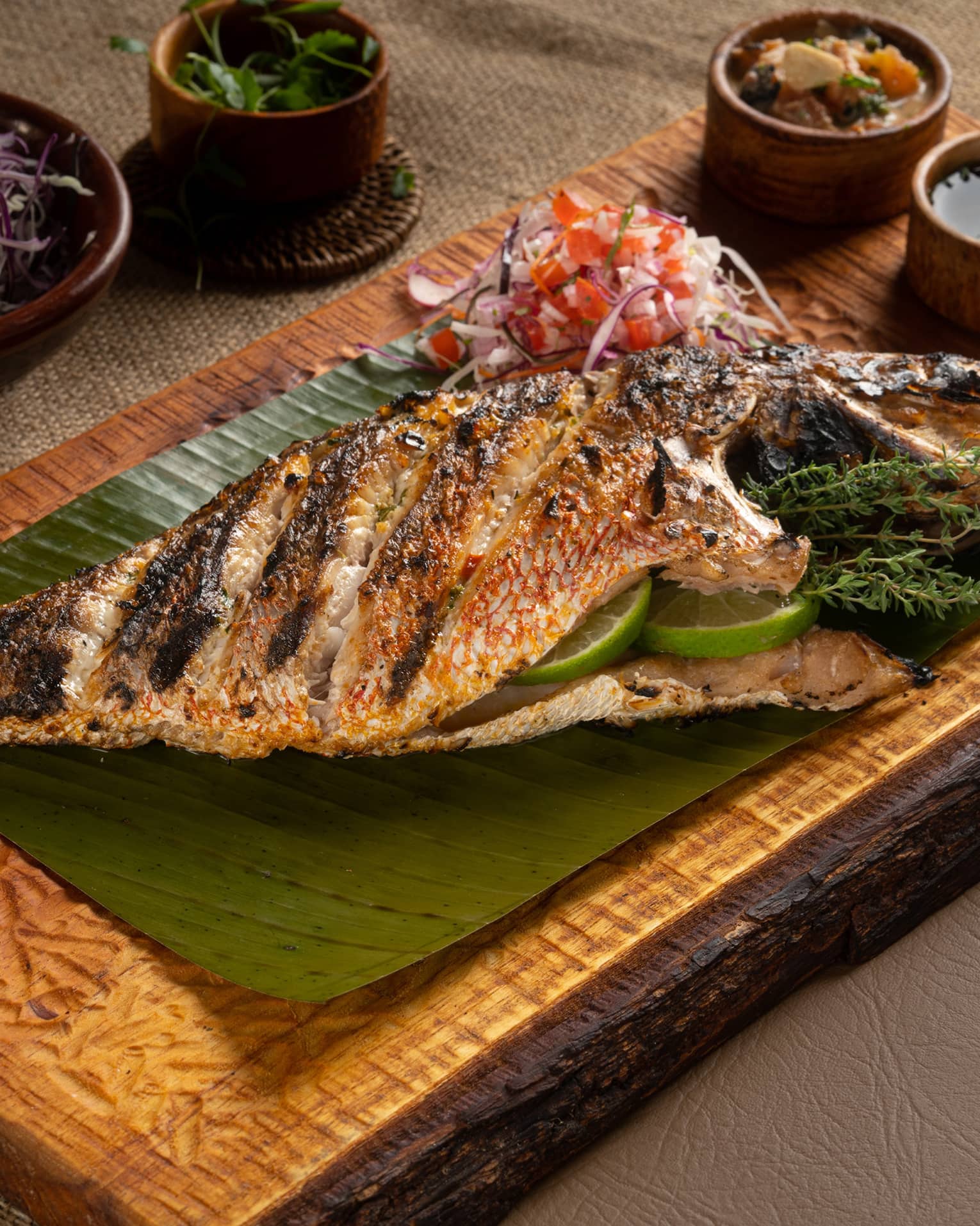 Whole Grilled Snapper served on a wooden plank along with an assortment of condiments and sauces
