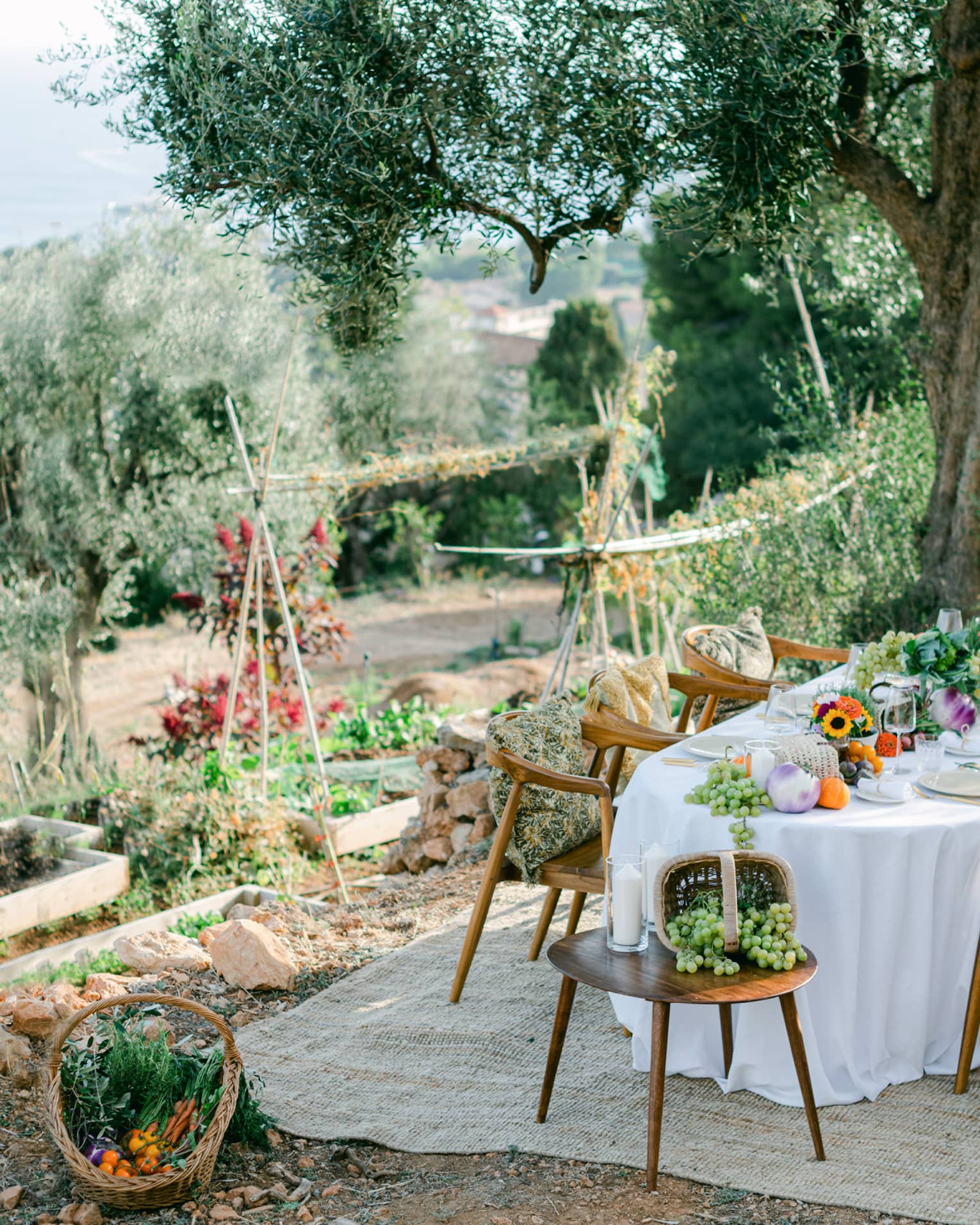 Garden dining setup with oval table draped in white and garden bounty down centre, and six chairs with pillows