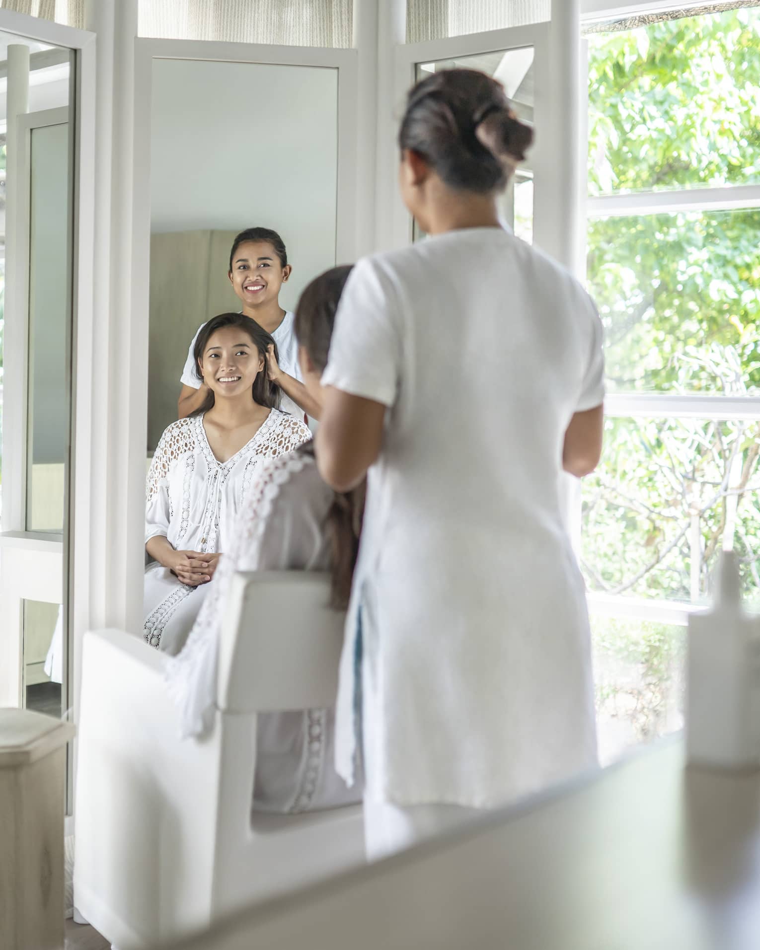 A stylist works on a woman's hair in light-filled salon