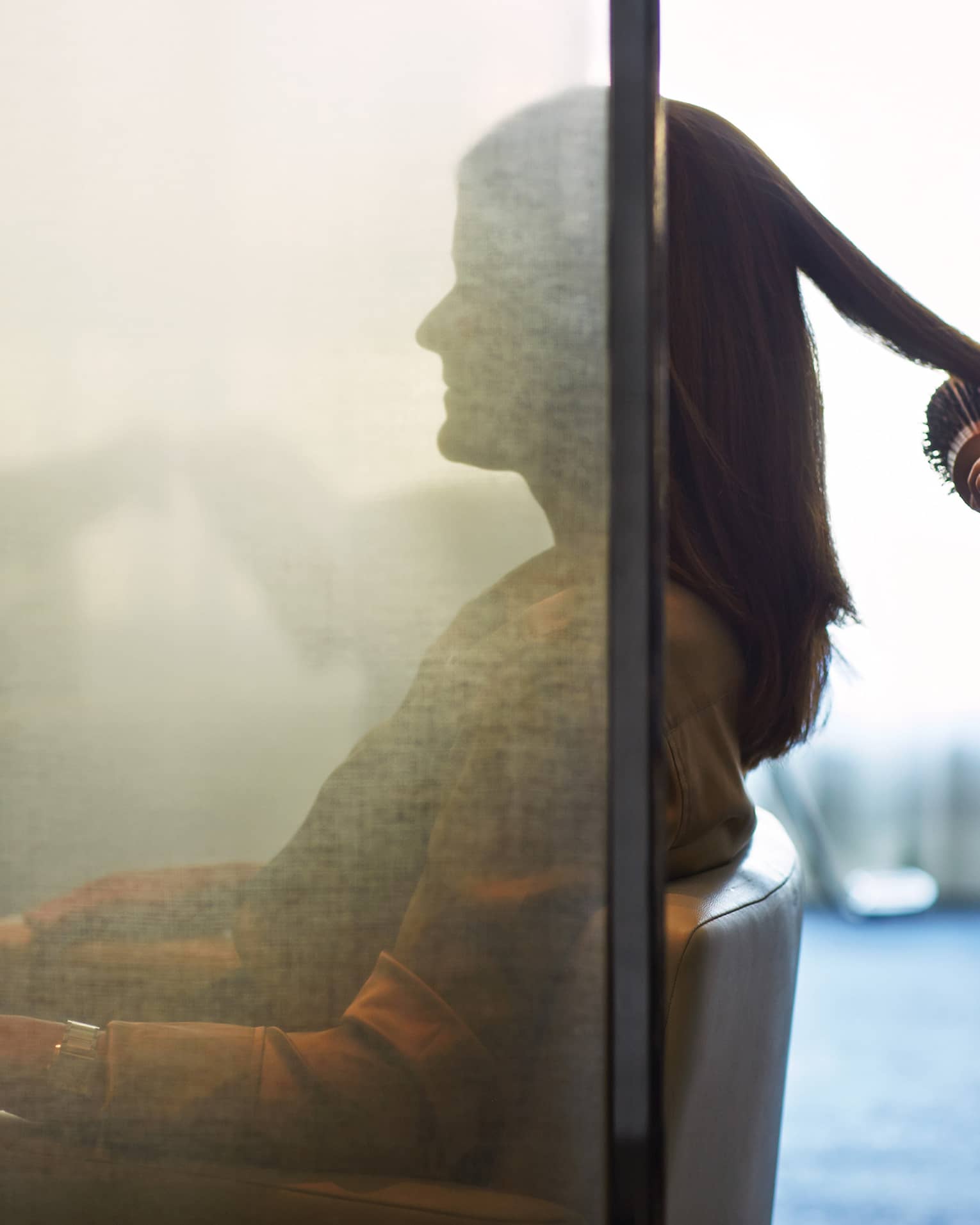 Silhouette of woman behind salon screen as hairdressers brushes, blow dries hair