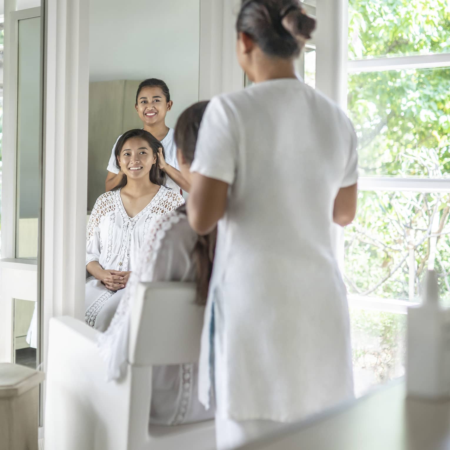 A stylist works on a woman's hair in light-filled salon