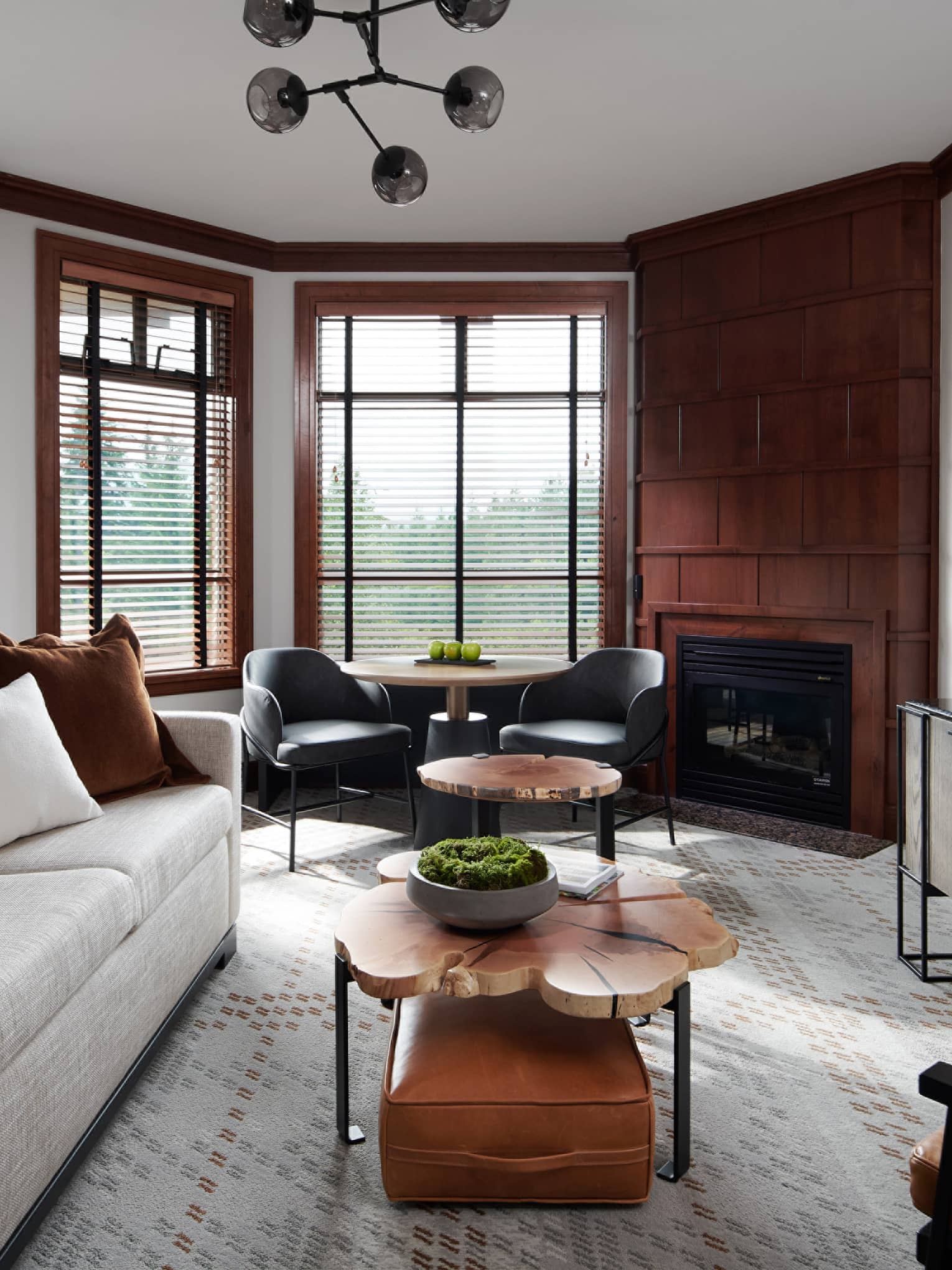 Sophisticated interior of a deluxe room at Four Seasons Whistler. The living space features elegant wood paneling, large windows with blinds, and a mix of modern furnishings including a plush gray sofa, leather armchairs, round wooden coffee tables, and a sleek black media console with a mounted flat-screen TV. A contemporary fireplace adds a cozy ambiance to the room.,Sophisticated interior of a deluxe room at Four Seasons Whistler. The living space features elegant wood paneling, large windows with blinds, and a mix of modern furnishings including a plush gray sofa, leather armchairs, round wooden coffee tables, and a sleek black media console with a mounted flat-screen TV. A contemporary fireplace adds a cozy ambiance to the room.