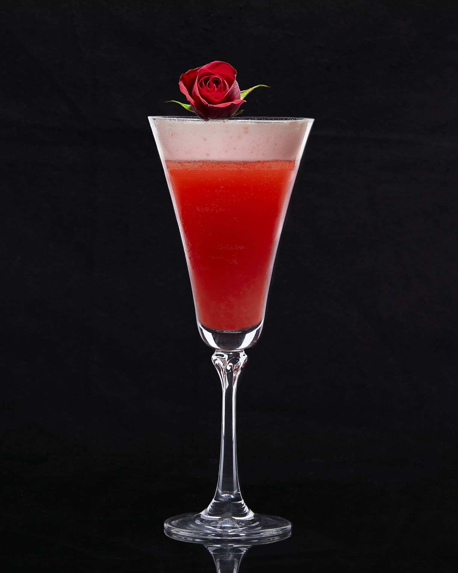 Cocktail glass with red drink and a rose on top.