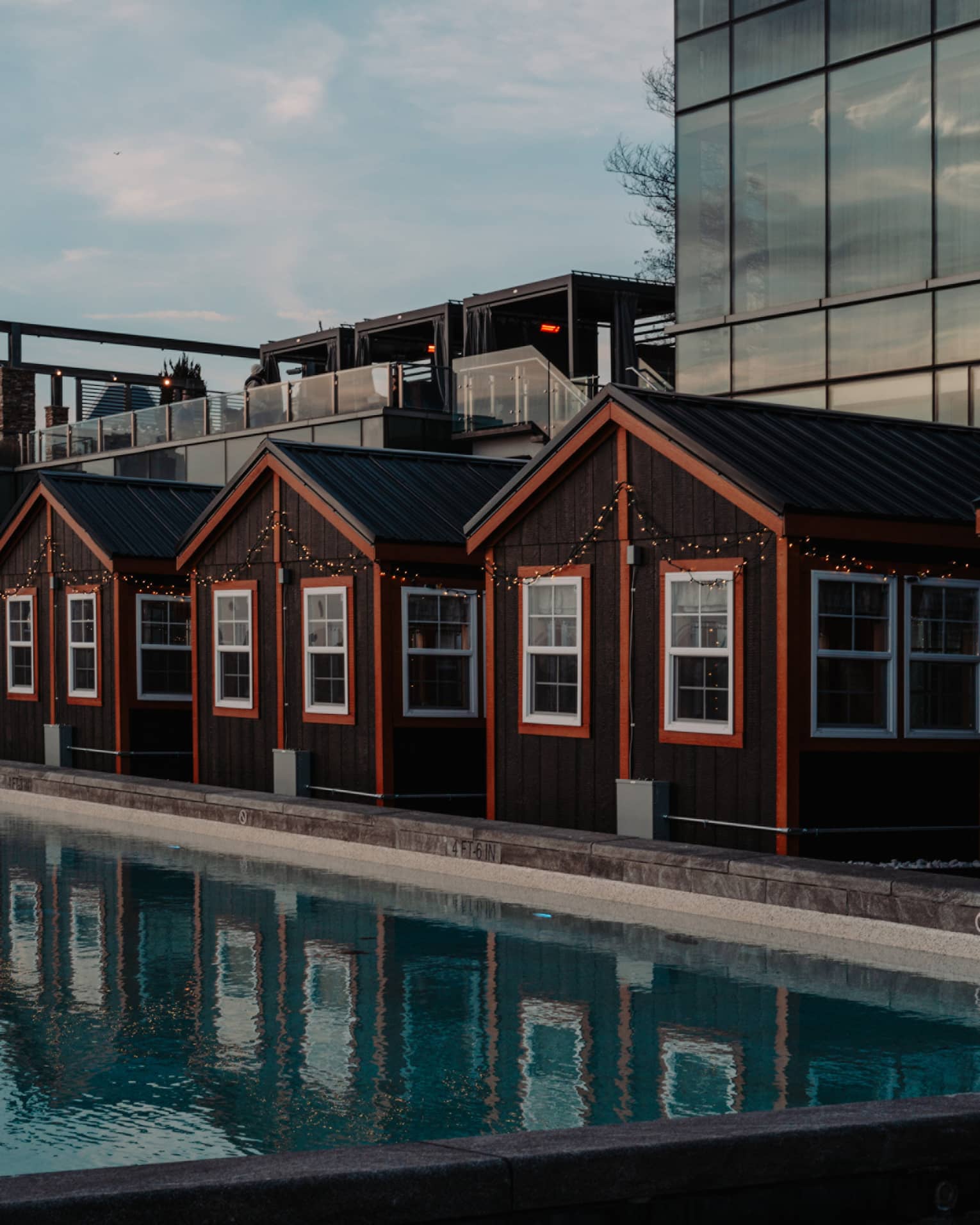 Four cottages with orange trimming beside a pool and city buildings